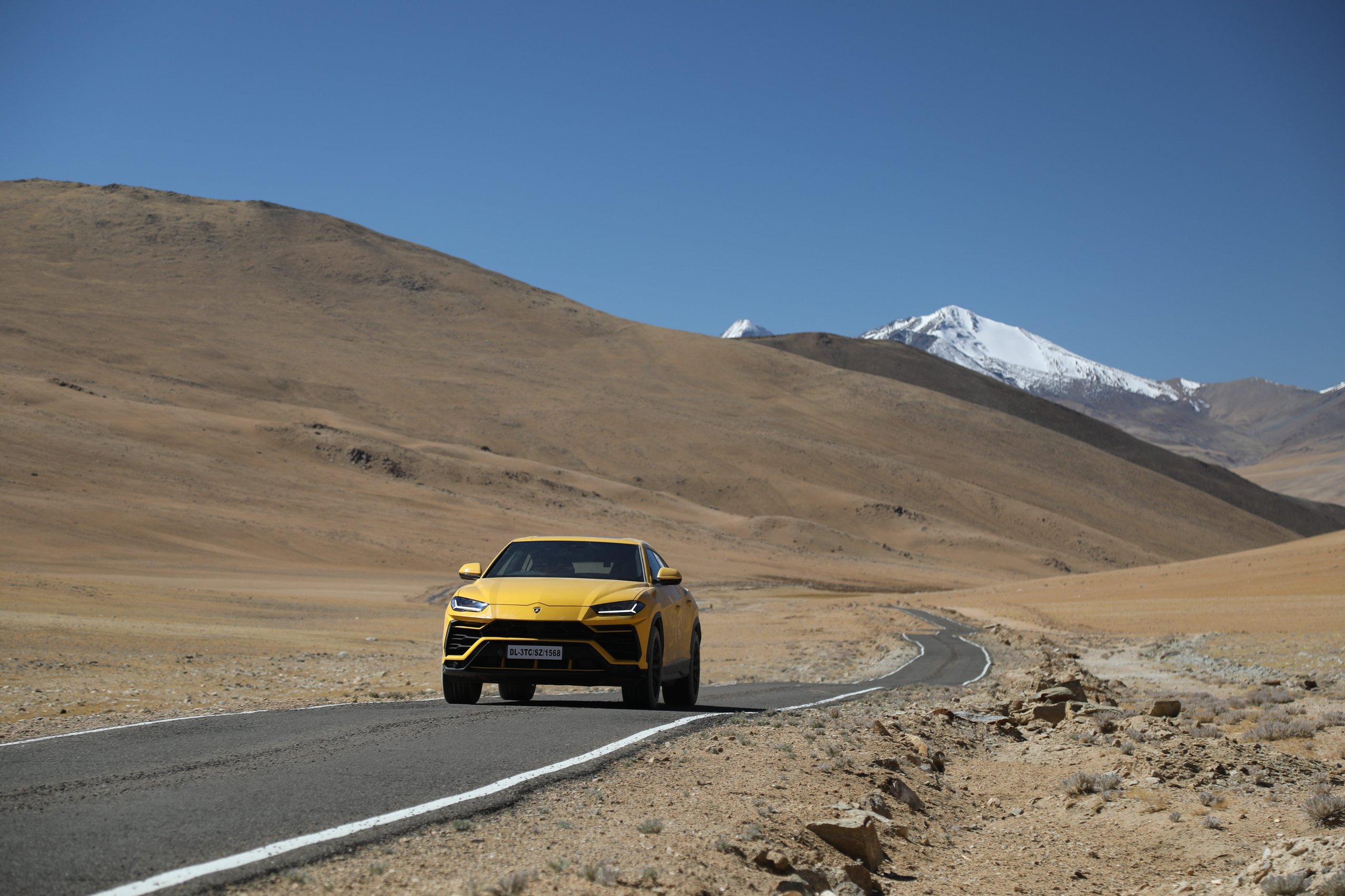The Lamborghini Urus At 19,300 Feet: Conquering The World'S Highest Drivable Road 11 Yellow lamborghini urus driving through an arid mountain landscape with a snow-capped peak in the distance