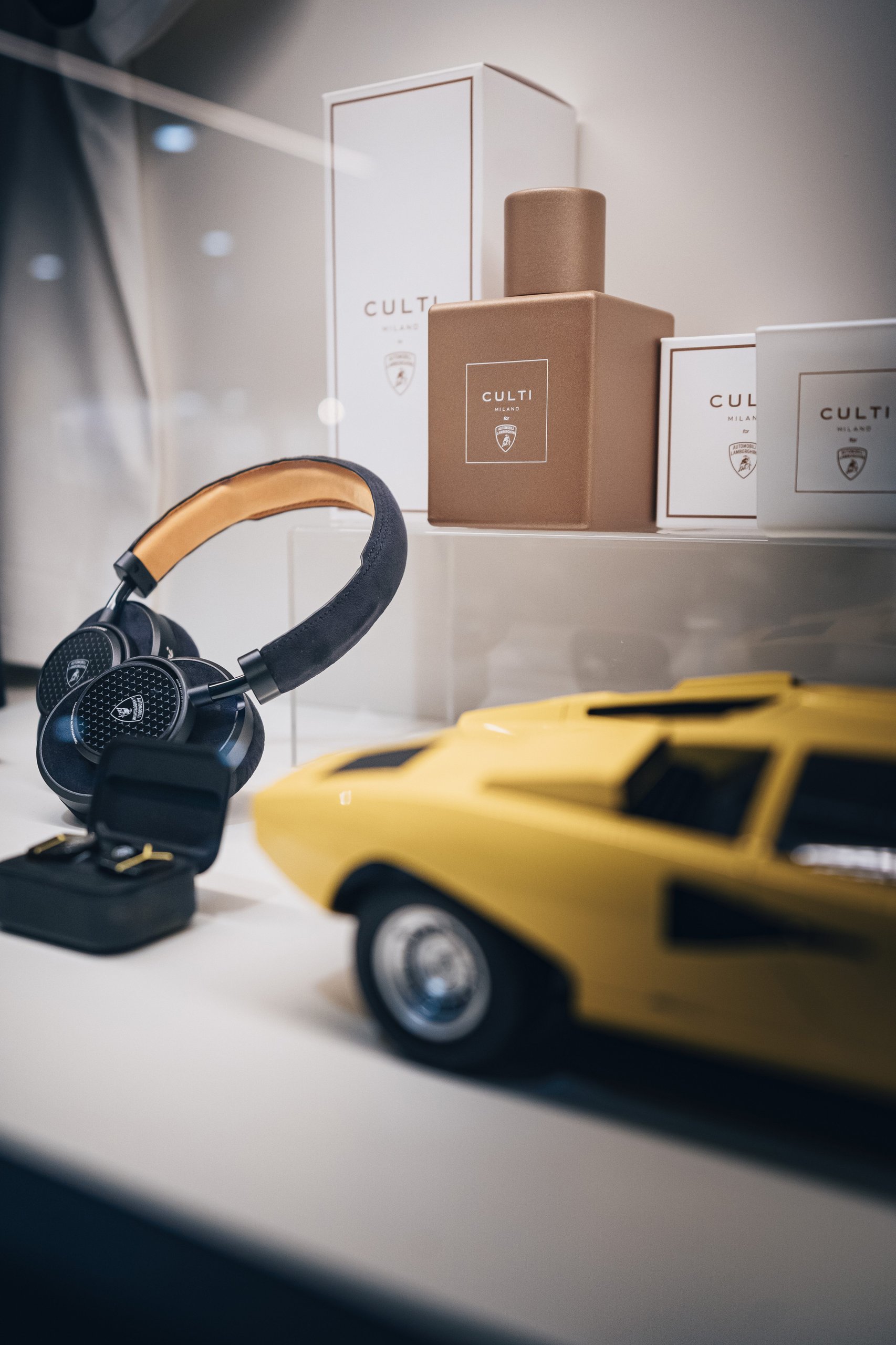 Lamborghini Turns Bologna Airport Into A Brand Experience, Complete With Urus Vip Shuttle And Huracán Follow-Me Car 7 Lamborghini-branded headphones displayed alongside a yellow countach model car and culti milano luxury products in the airport boutique