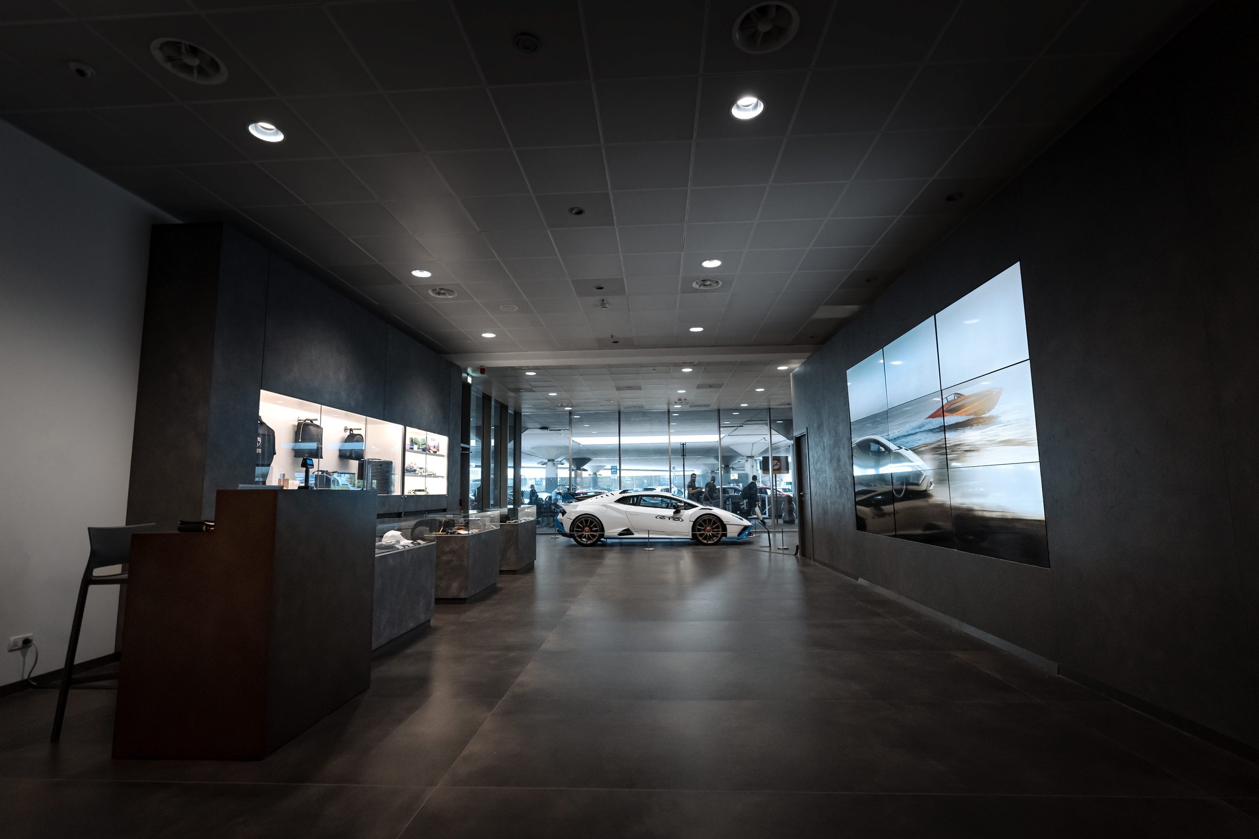 Lamborghini Turns Bologna Airport Into A Brand Experience, Complete With Urus Vip Shuttle And Huracán Follow-Me Car 3 Wide shot of the lamborghini boutique inside bologna airport terminal, featuring a white huracán sto, branded merchandise, and a digital display screen