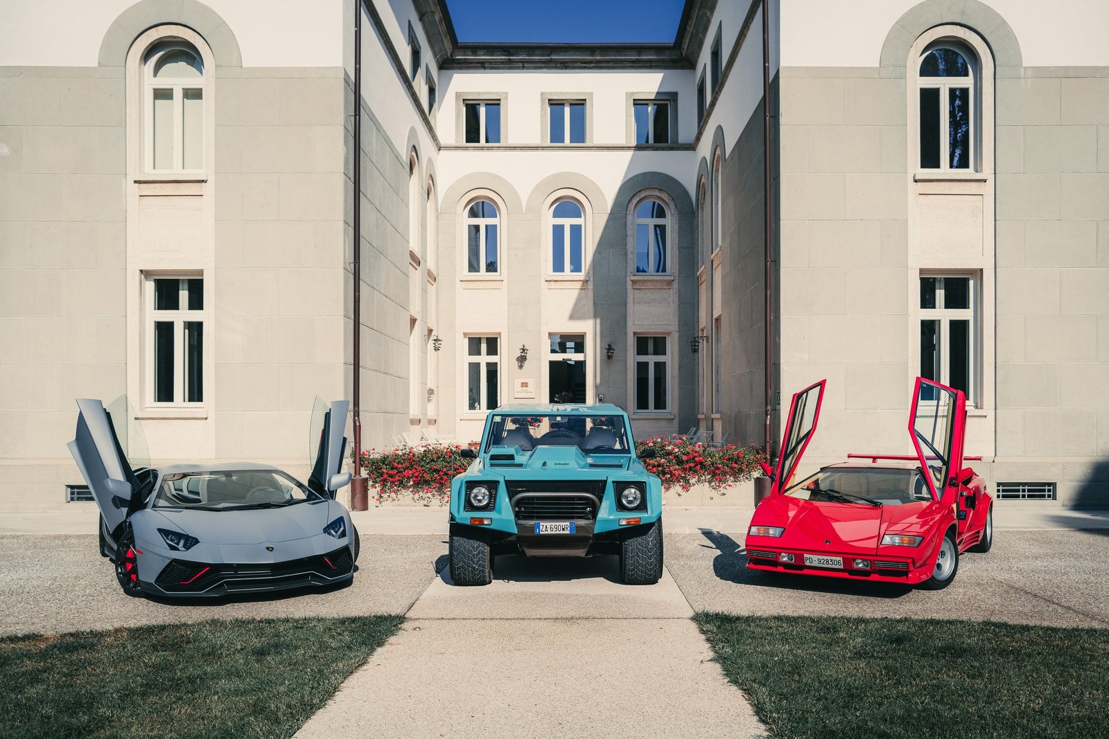 Lamborghini Aventador SVJ, LM 002, and Countach parked together in front of a grand building with doors open, showcasing V12 heritage across eras