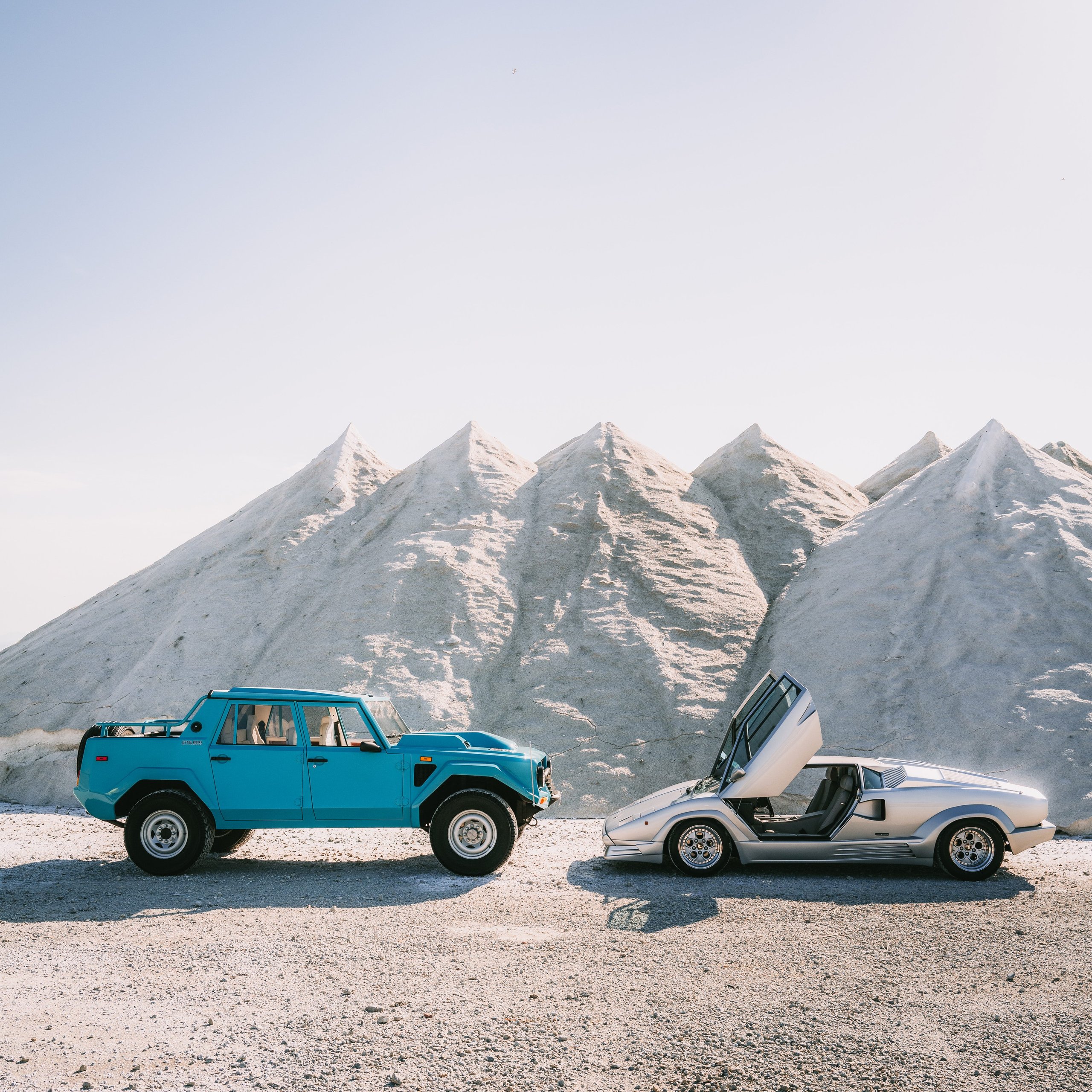 One V12, Two Wildly Different Lamborghinis: How The Countach And Lm 002 Proved The Twelve-Cylinder Could Do Anything 11 Silver lamborghini countach with scissor doors open alongside teal lm 002 in a desolate sandy landscape with white mounds