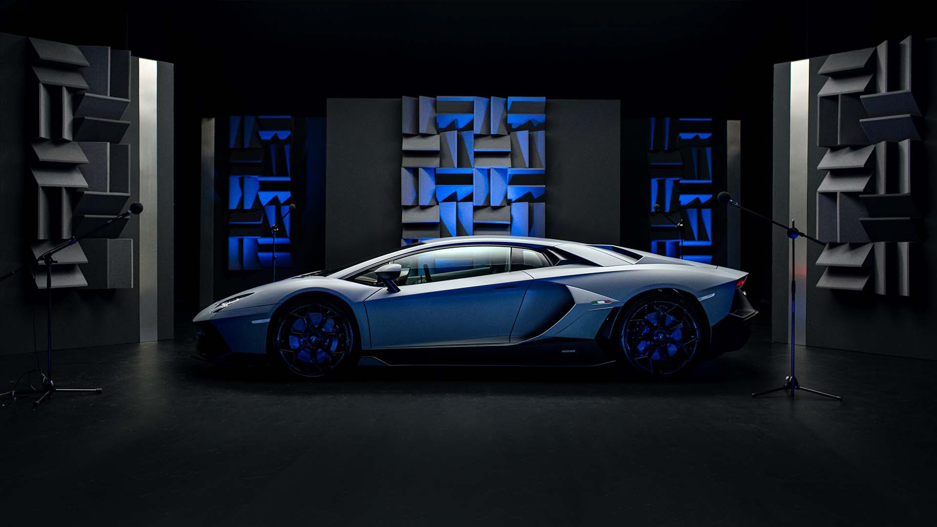 Grey lamborghini aventador in a dark studio surrounded by microphones and blue-lit sound-absorbing panels