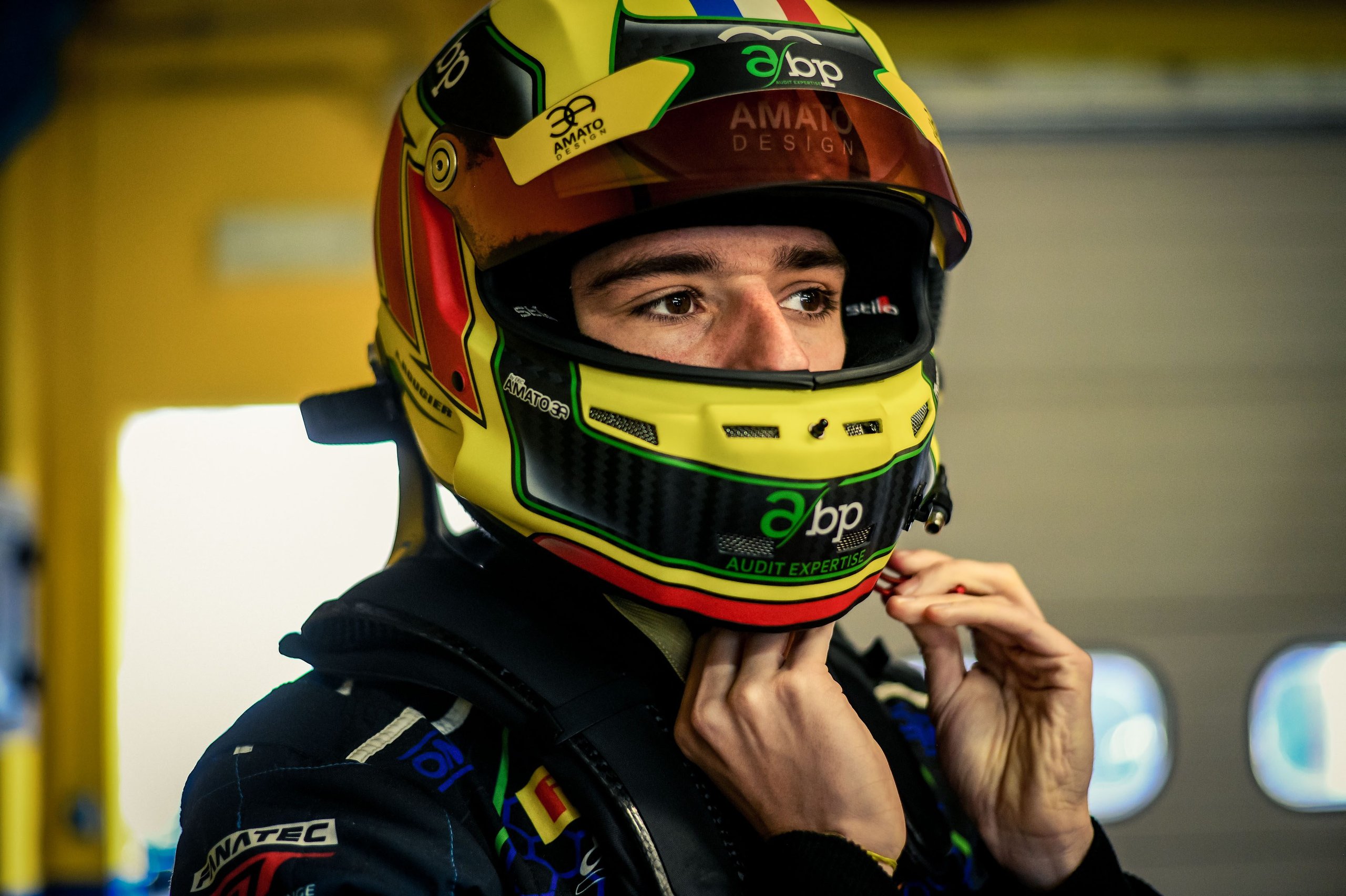Close-up portrait of a young lamborghini race driver in a yellow and black helmet adjusting his chin strap in a pit garage