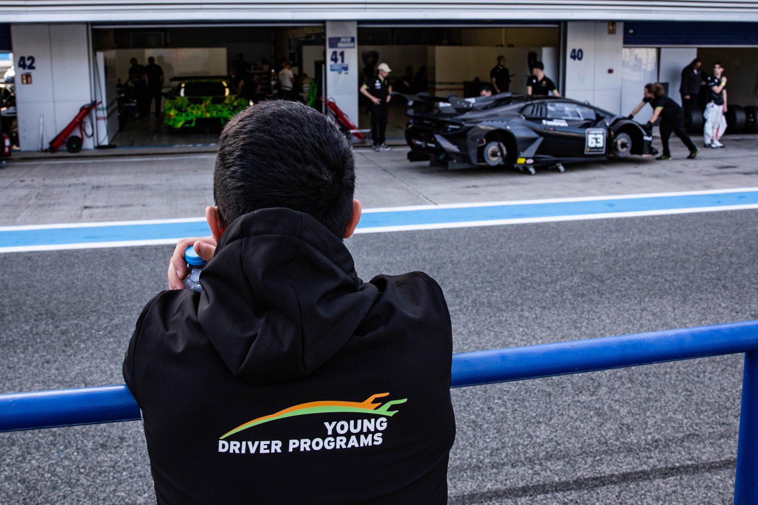 Squadra Corse Rewrites Its Talent Playbook: 26 Drivers Enter Lamborghini'S Merit-Based Pipeline For 2025 5 A person in a young driver programs hoodie observing lamborghini race cars in pit garages