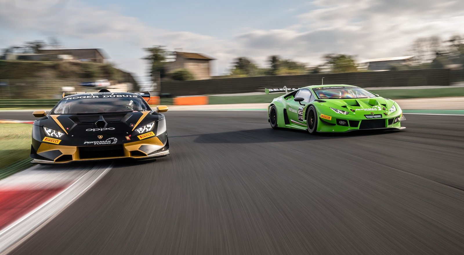 Two Lamborghini Huracán GT3 Evo race cars battle side-by-side on track under cloudy skies