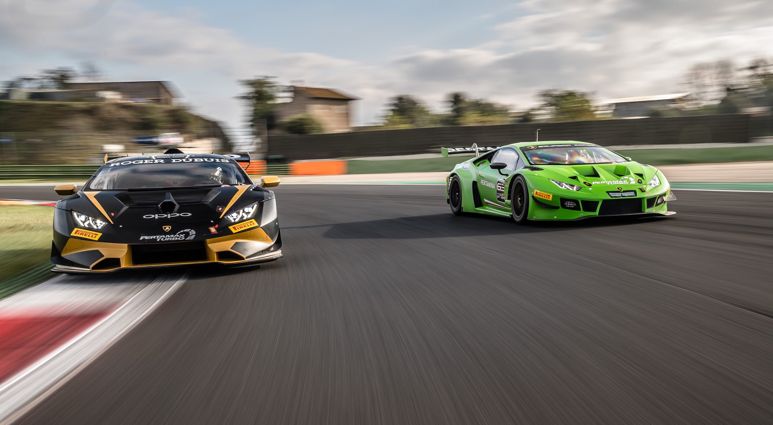 Two lamborghini huracán gt3 evo race cars battle side-by-side on track under cloudy skies
