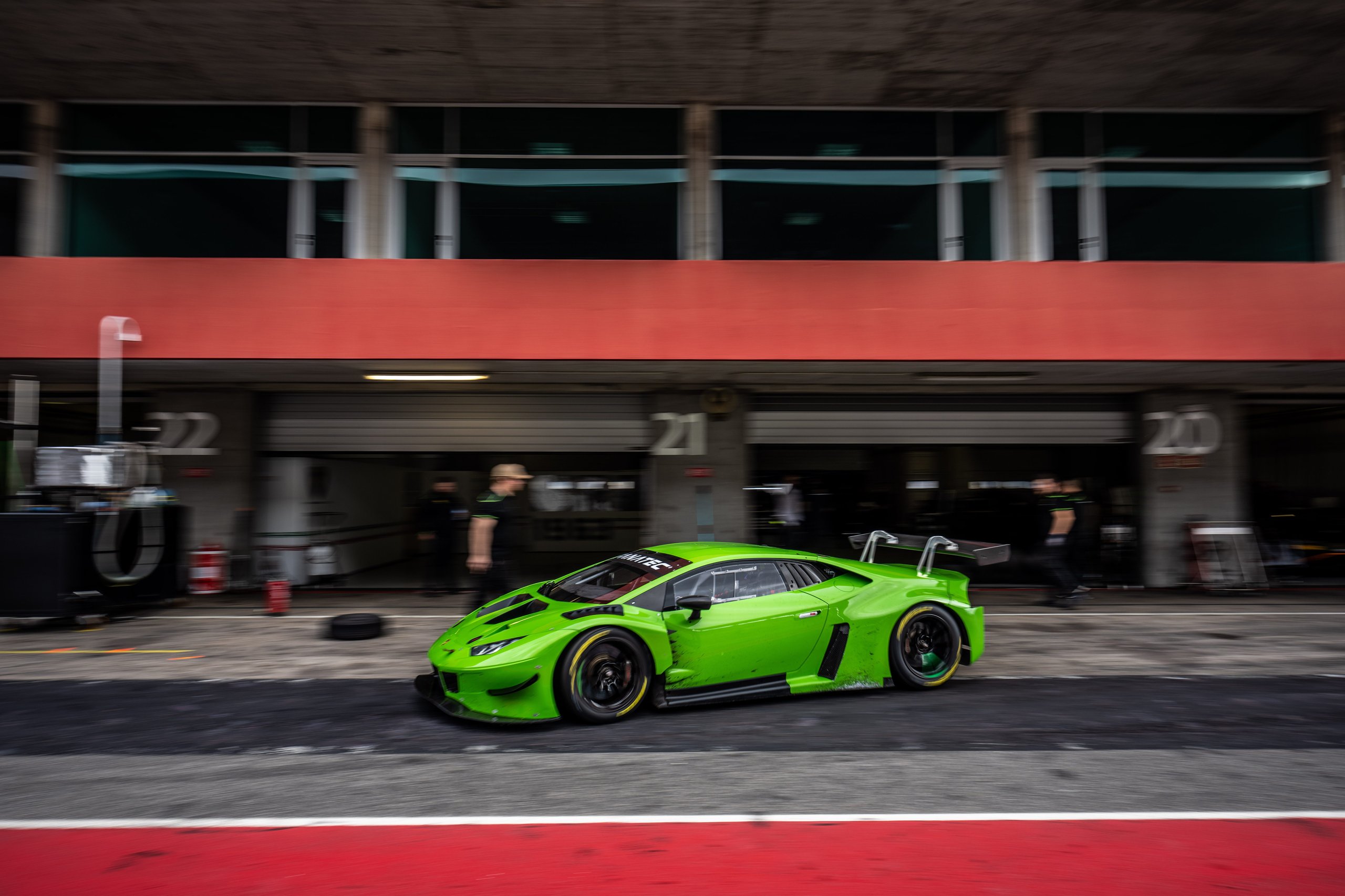 A bright green lamborghini huracán super trofeo evo2 race car in motion on a circuit with pit lane in the background