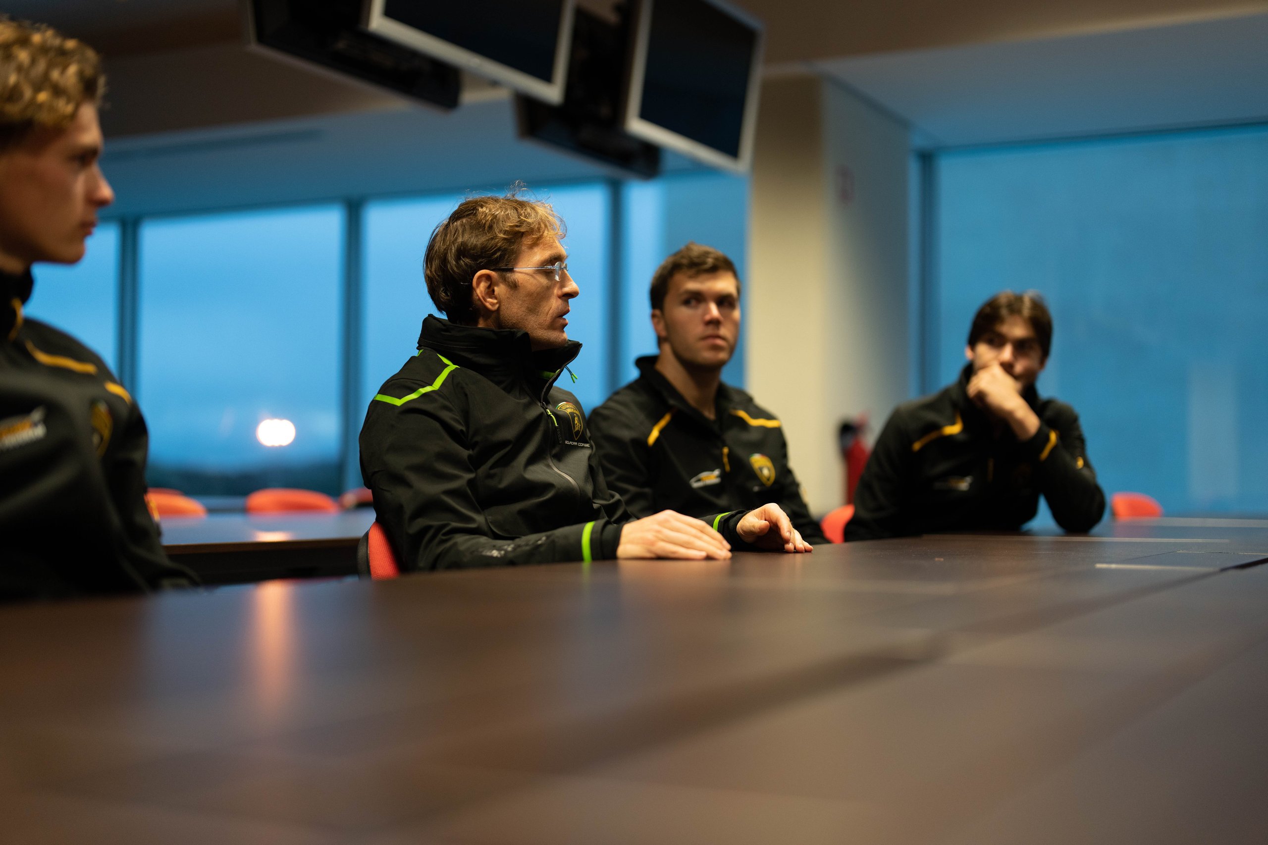 Young lamborghini squadra corse drivers seated around a conference table during a classroom briefing session