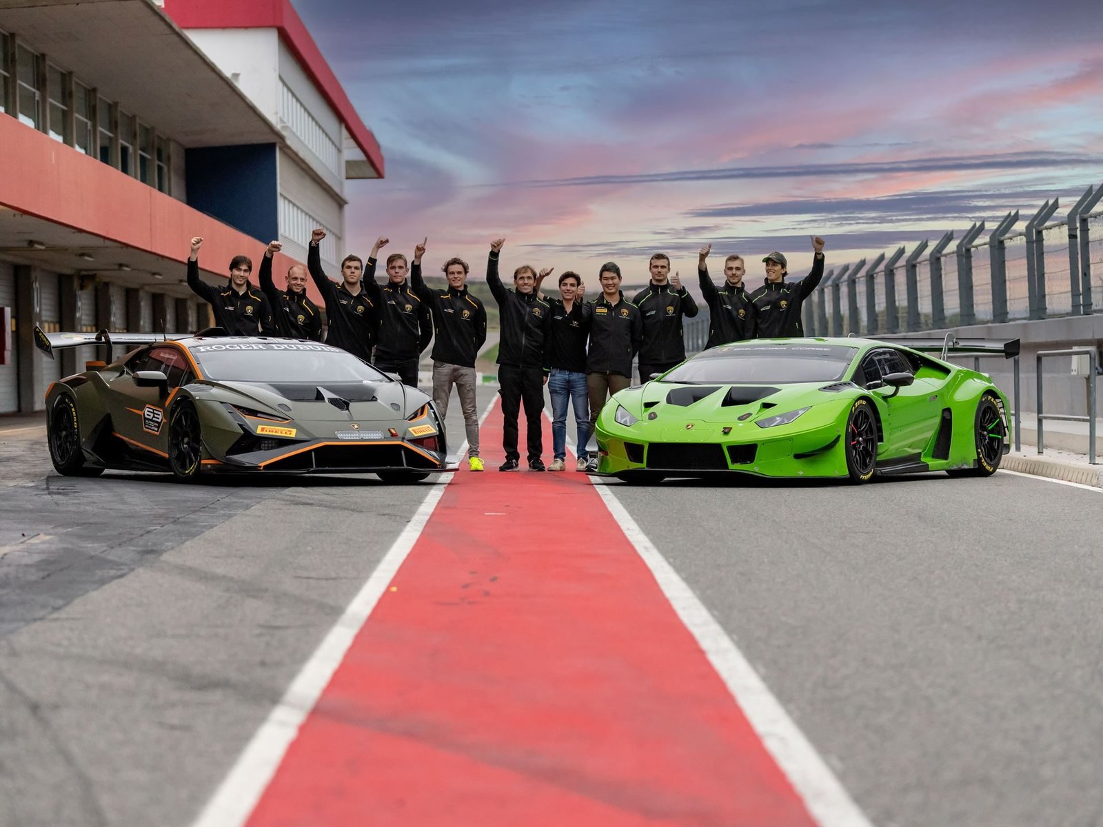 Lamborghini Squadra Corse drivers and team members celebrate in front of two Huracán Super Trofeo EVO2 race cars on a circuit pit lane