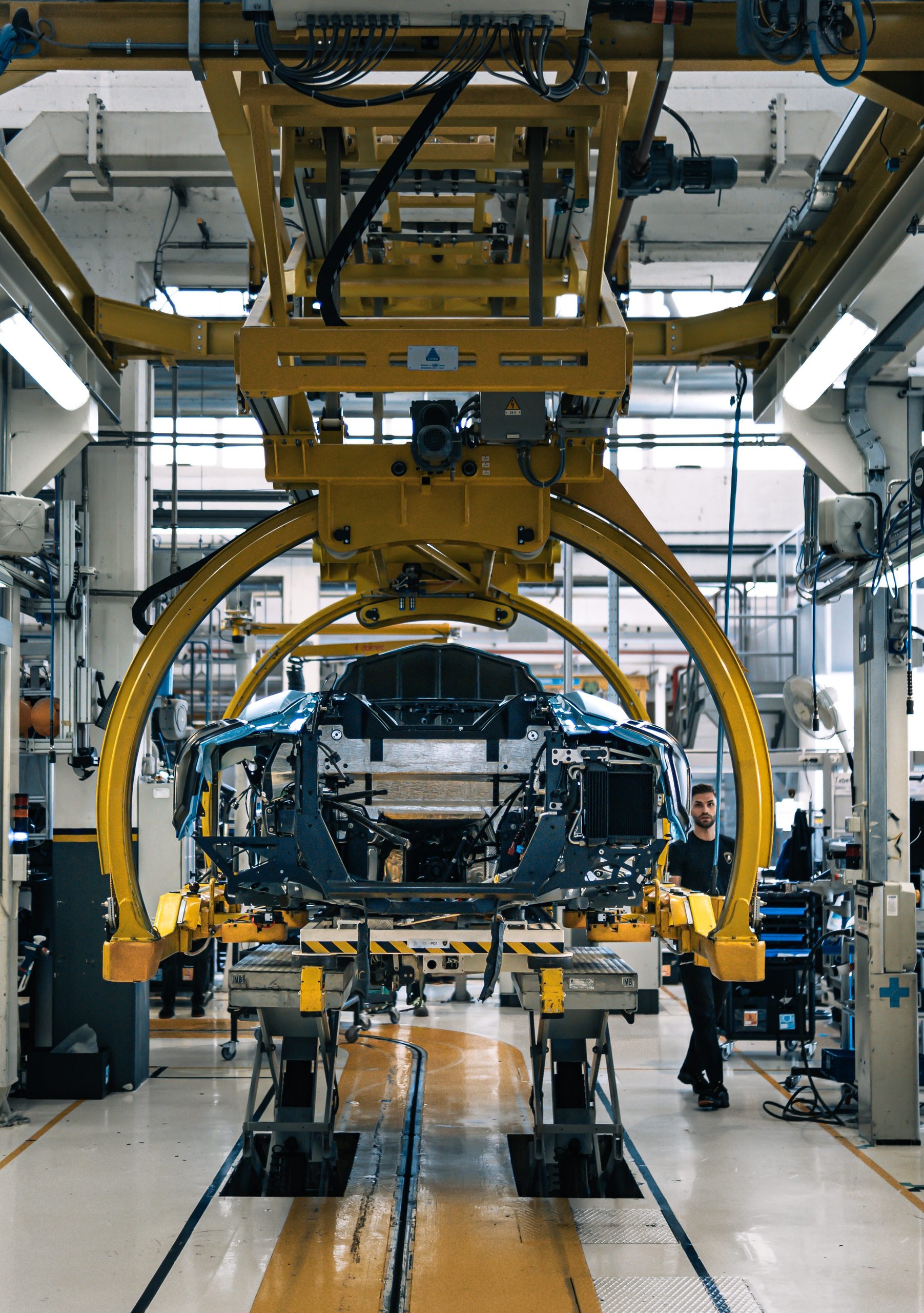 The Last Pure V12 Lamborghini Rolled Off The Line In Light Blue, And Nothing Will Replace What It Represented 7 Lamborghini aventador carbon fiber monocoque chassis suspended on assembly line under a yellow gantry