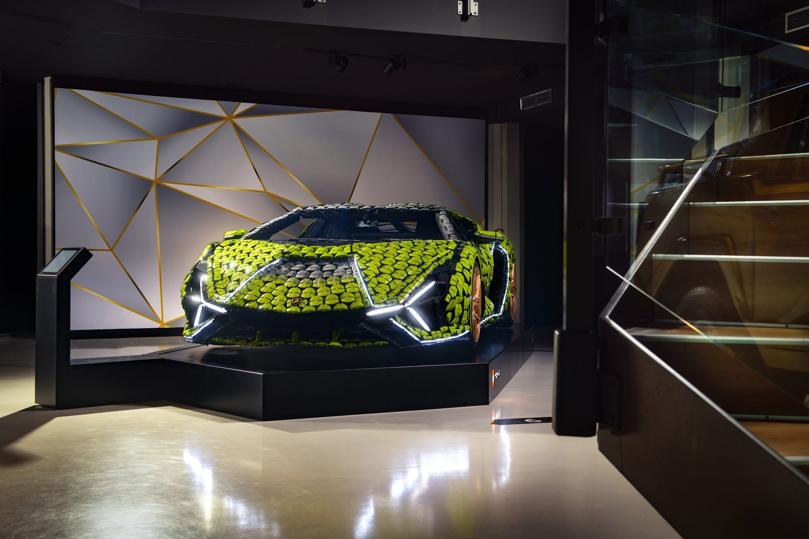 Full front three-quarter view of the life-size LEGO Technic Lamborghini Sián FKP 37 on display at Museo Automobili Lamborghini, showing its lime green and black brick body, illuminated headlights, and bronze wheels.