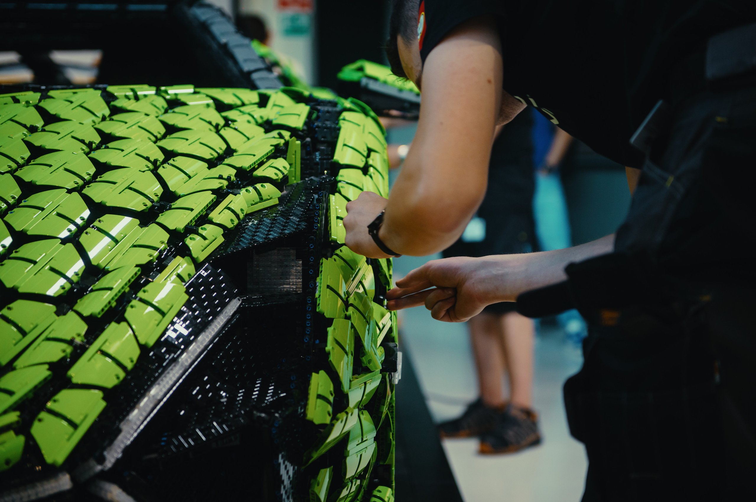 400,000 Bricks, One Sián: Inside The Life-Size Lego Technic Lamborghini That Got Painted In Sant'Agata 3 Close-up of hands assembling lime green and black lego technic bricks on the life-size lamborghini sián fkp 37 model, showing the hexagonal brick pattern.