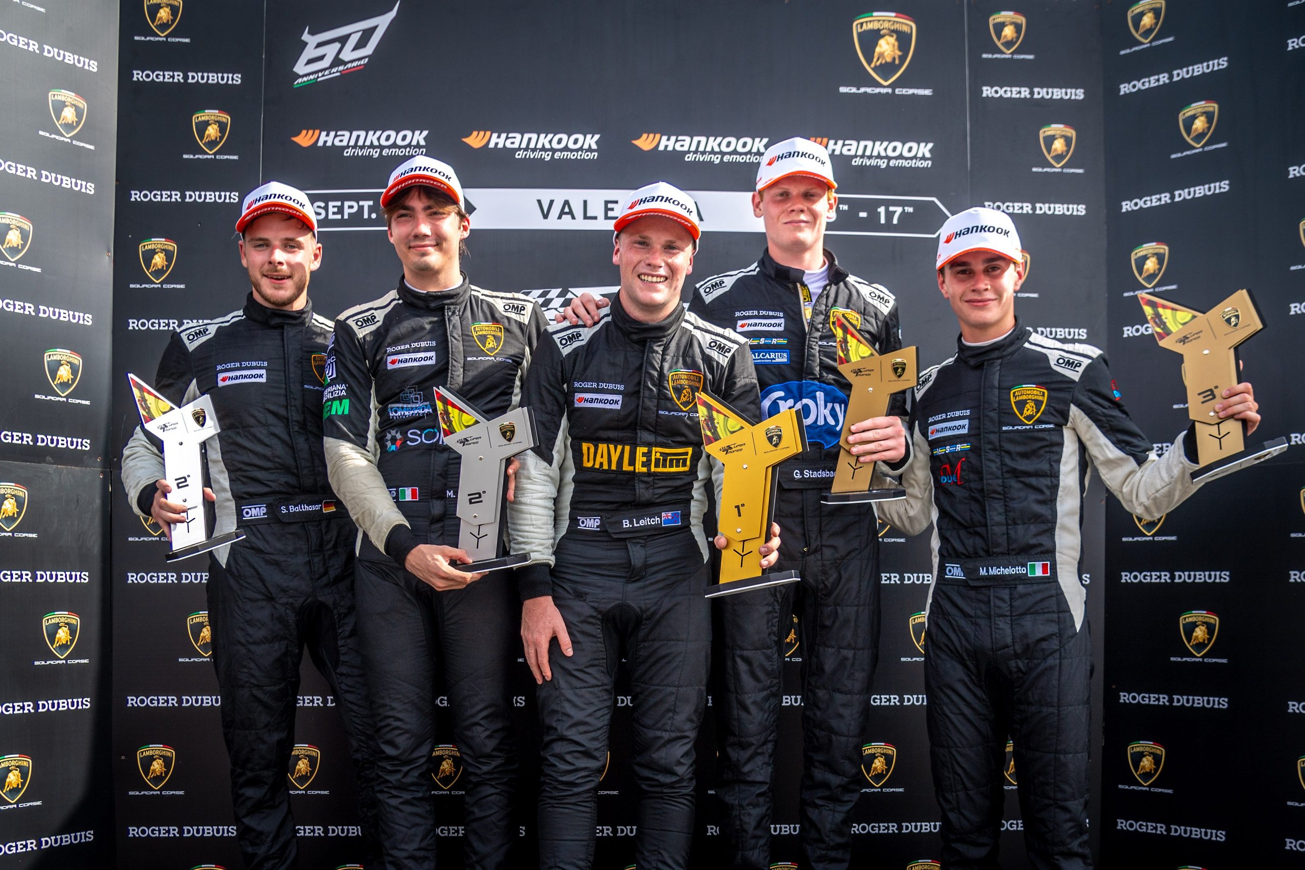 Five lamborghini super trofeo europe drivers celebrate on the podium holding trophies against a branded backdrop
