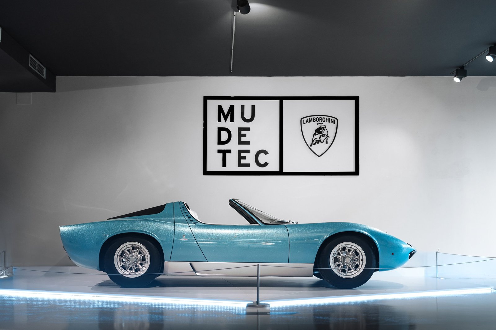 Full side profile of the light blue metallic 1968 Lamborghini Miura Roadster on display at the MUDETEC museum, illuminated by floor lighting