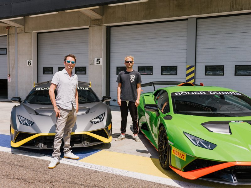 Matt Bellamy and Dom Howard of Muse standing in the pit lane with grey and green Lamborghini Huracán STO cars bearing Squadra Corse livery