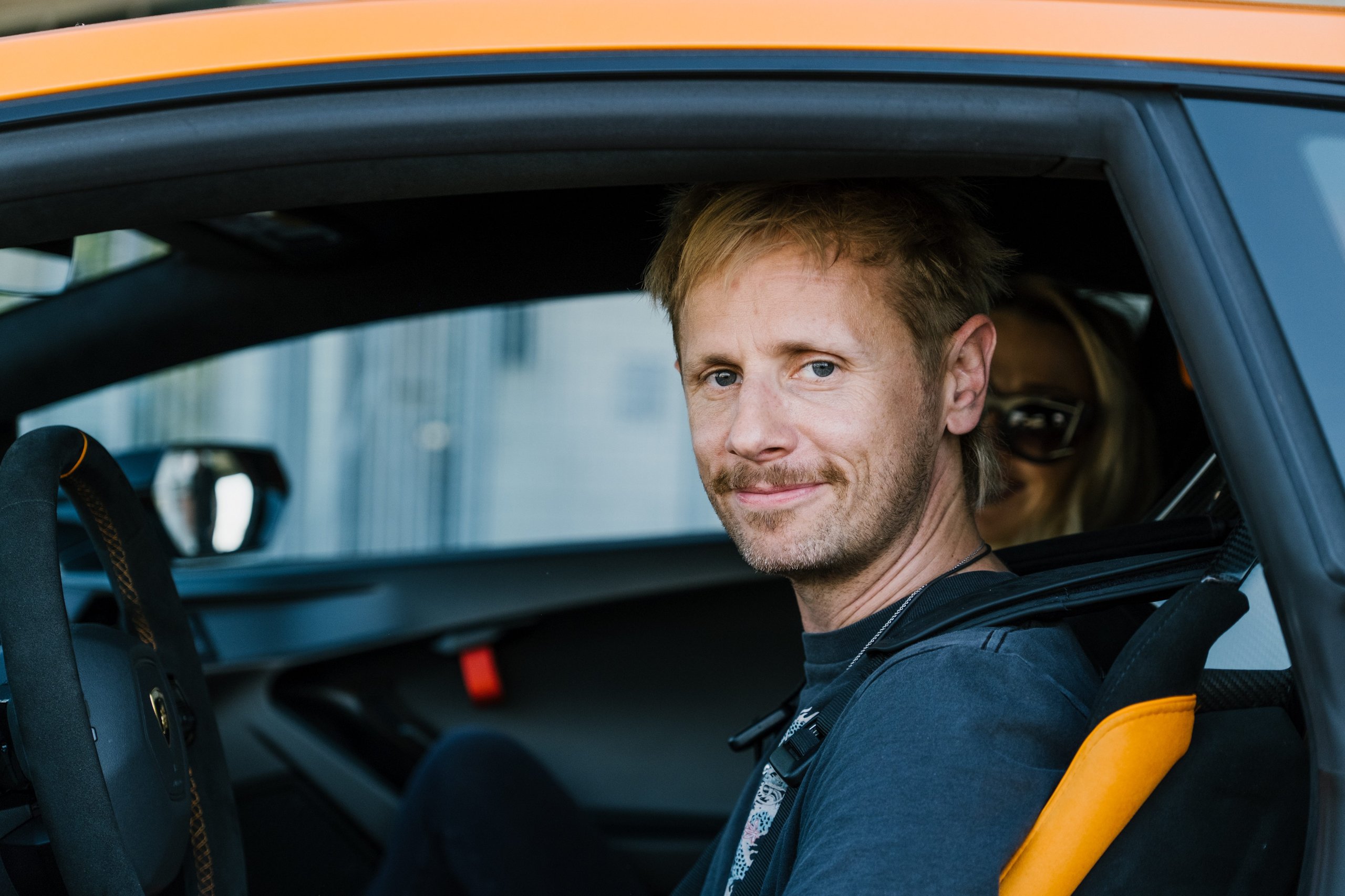 When Muse Visited Sant'Agata, The Huracán Sto Became Their Opening Act 7 Dom howard seated in the passenger seat of an orange lamborghini huracán sto with racing harness visible