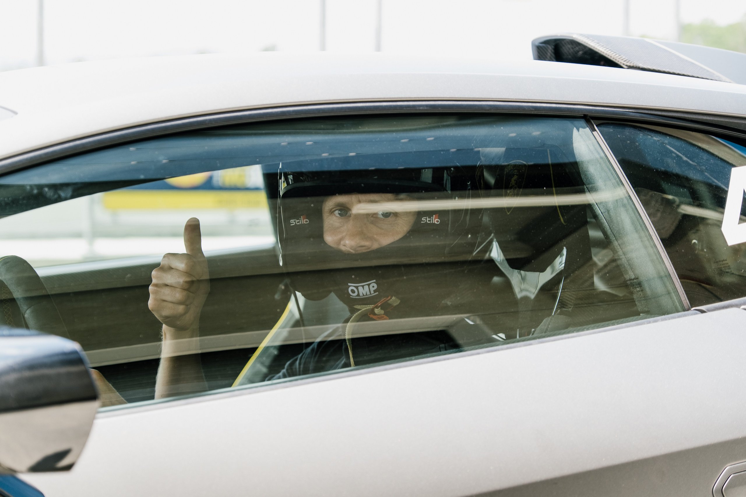 When Muse Visited Sant'Agata, The Huracán Sto Became Their Opening Act 11 A person in racing helmet and suit giving a thumbs-up from inside a silver lamborghini huracán sto