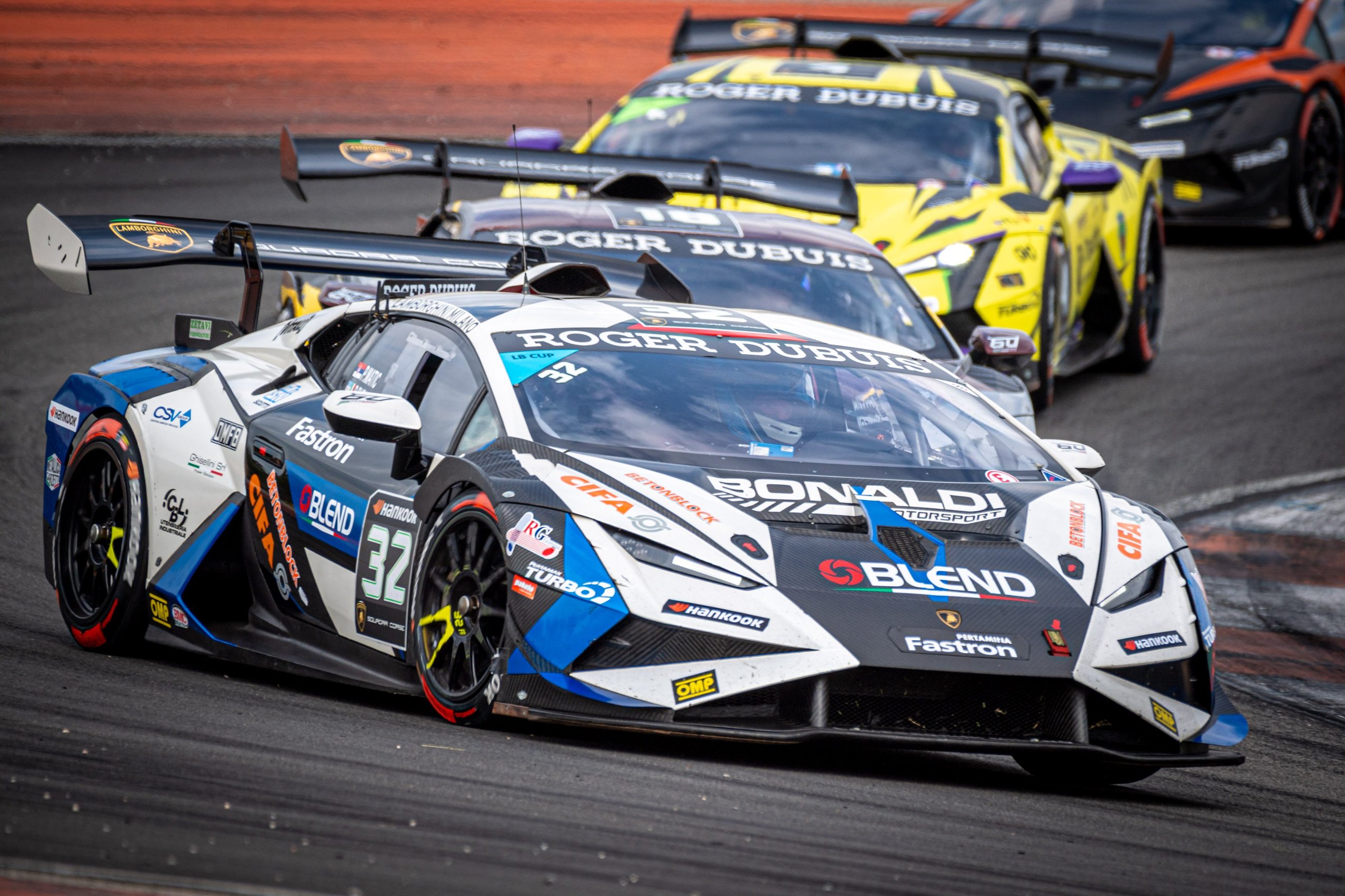 A white, blue, and black Lamborghini Huracán Super Trofeo EVO2 leads two competitors through a corner at Valencia
