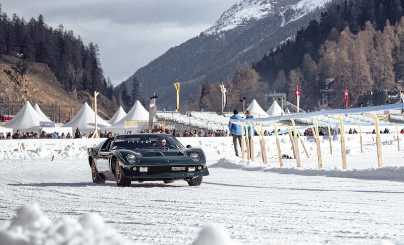 Dark green Lamborghini Miura P400 S Millechiodi driving on a snowy track at THE ICE Concours d'Elegance in St. Moritz with spectators and mountains in the background