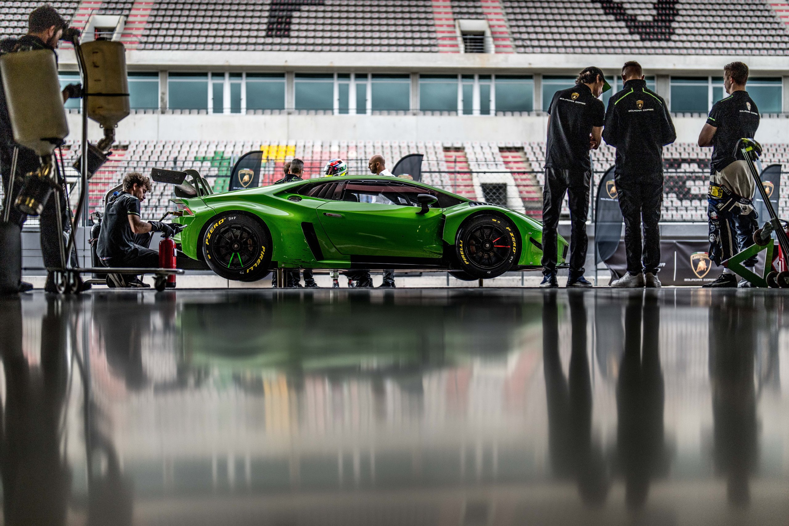 Green lamborghini huracán gt3 evo2 raised on jacks in the pit lane with mechanics preparing the car for the shootout