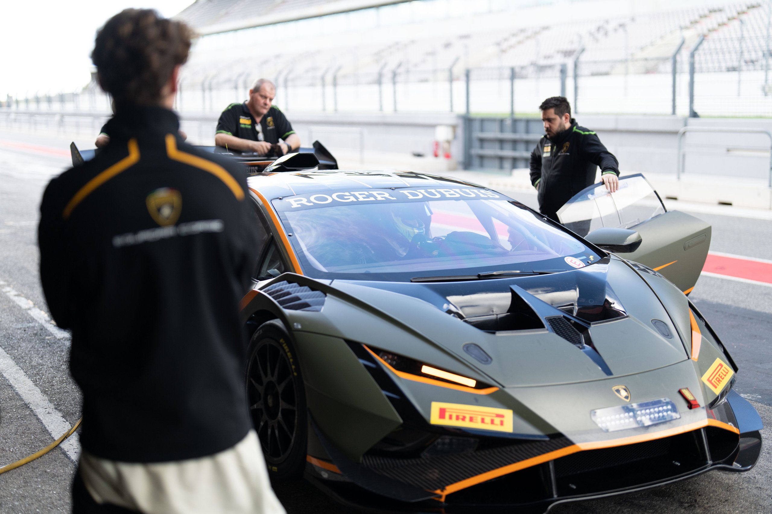 Matte grey lamborghini huracán gt3 evo2 in the portimão pit lane with team members conducting final preparations