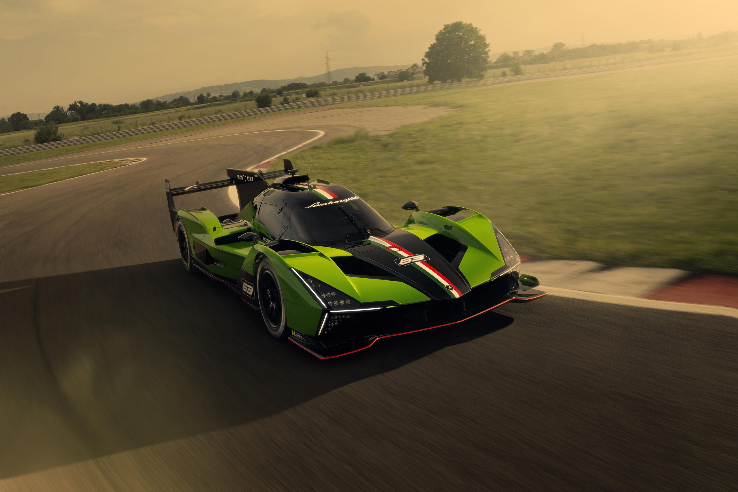 Green and black Lamborghini SC63 race car speeding around a track corner at sunset