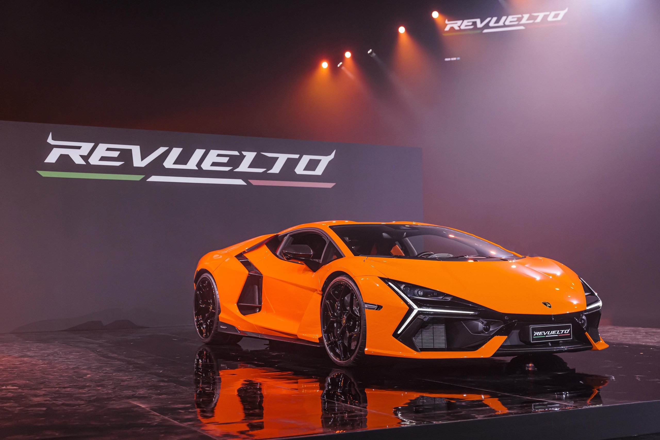 Orange Lamborghini Revuelto unveiled on stage with REVUELTO branding illuminated behind it