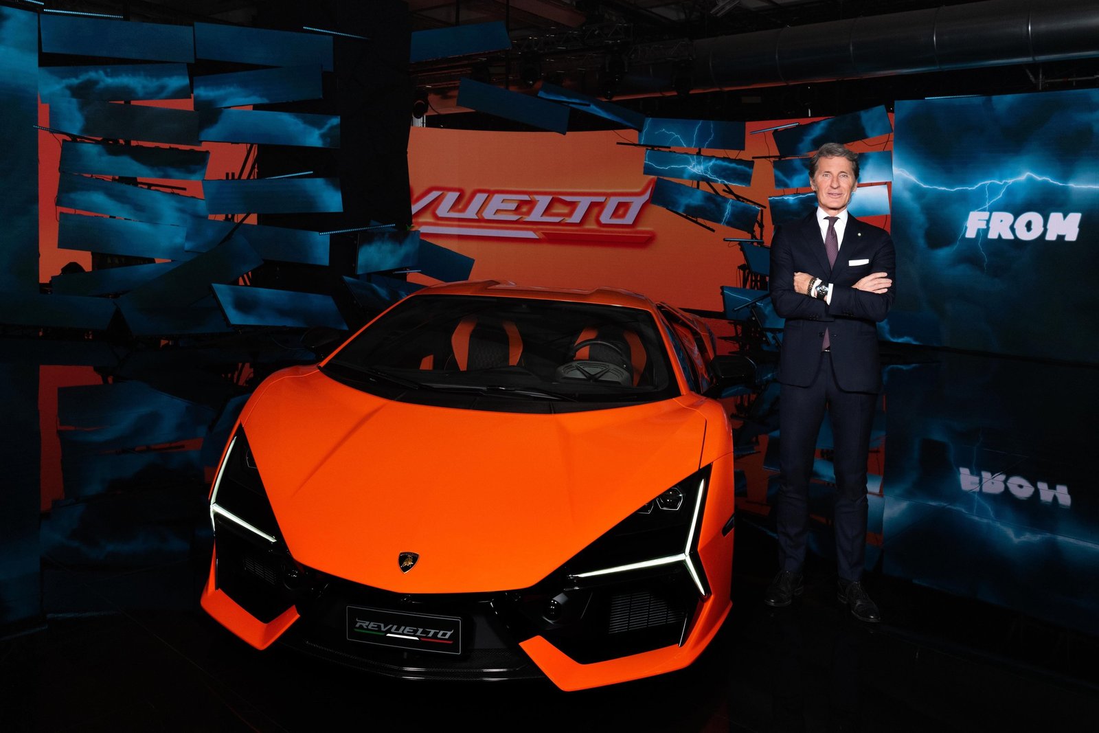 Stephan Winkelmann standing beside the orange Lamborghini Revuelto at its official reveal event