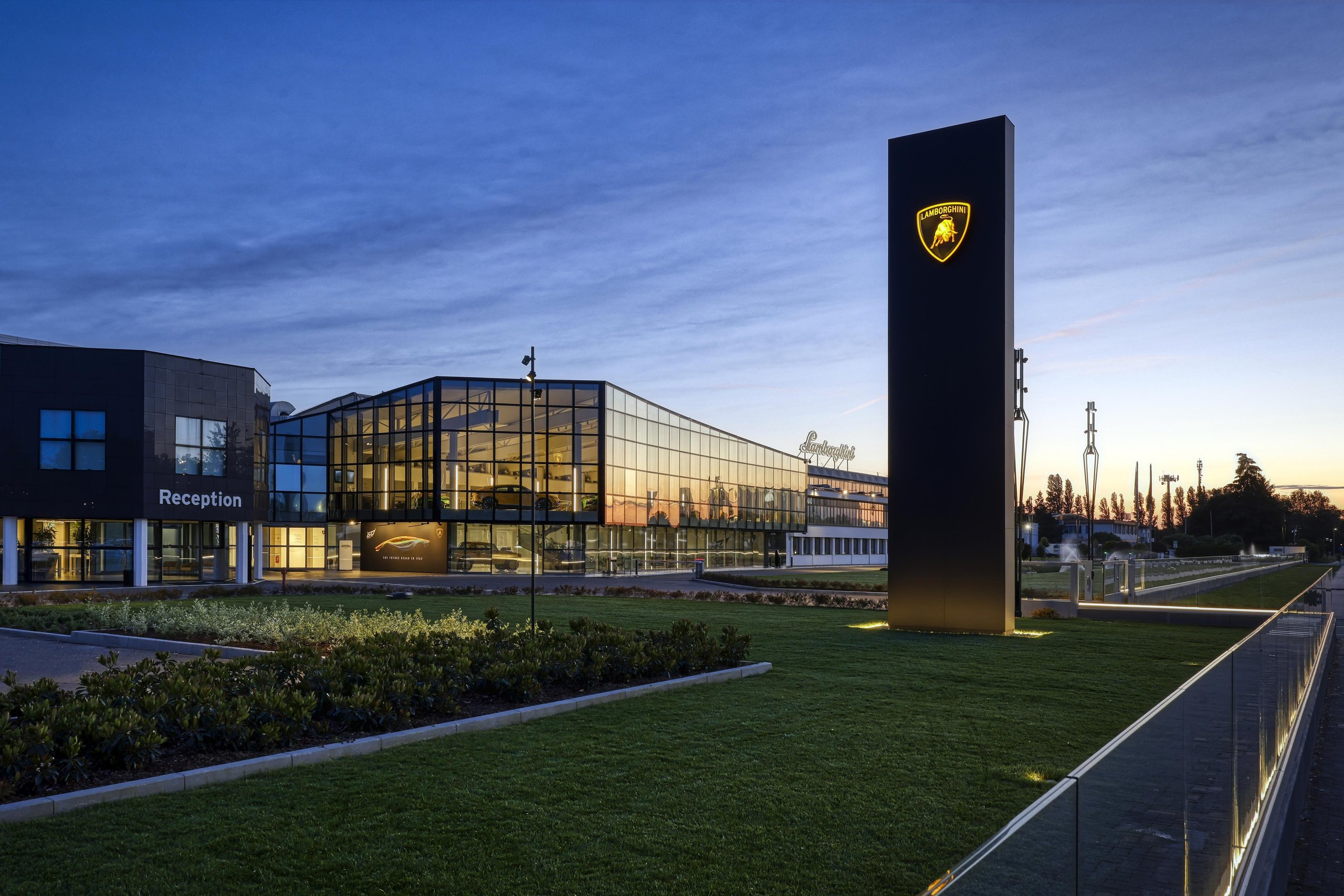 Evening shot of the Lamborghini factory entrance with illuminated logo on a black pillar