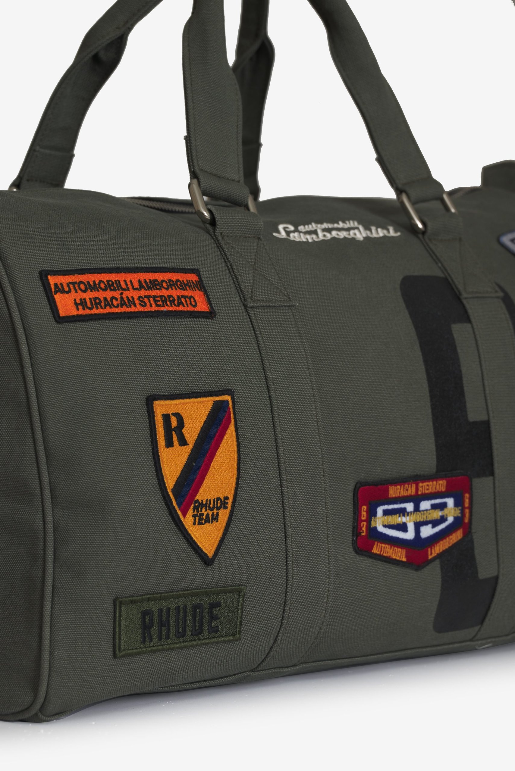 Rhude X Automobili Lamborghini: A Sterrato-Inspired Capsule That Reveals Where The Brand Is Headed 11 Olive green canvas duffel bag from the rhude x automobili lamborghini collection, featuring embroidered huracán sterrato and rhude team patches
