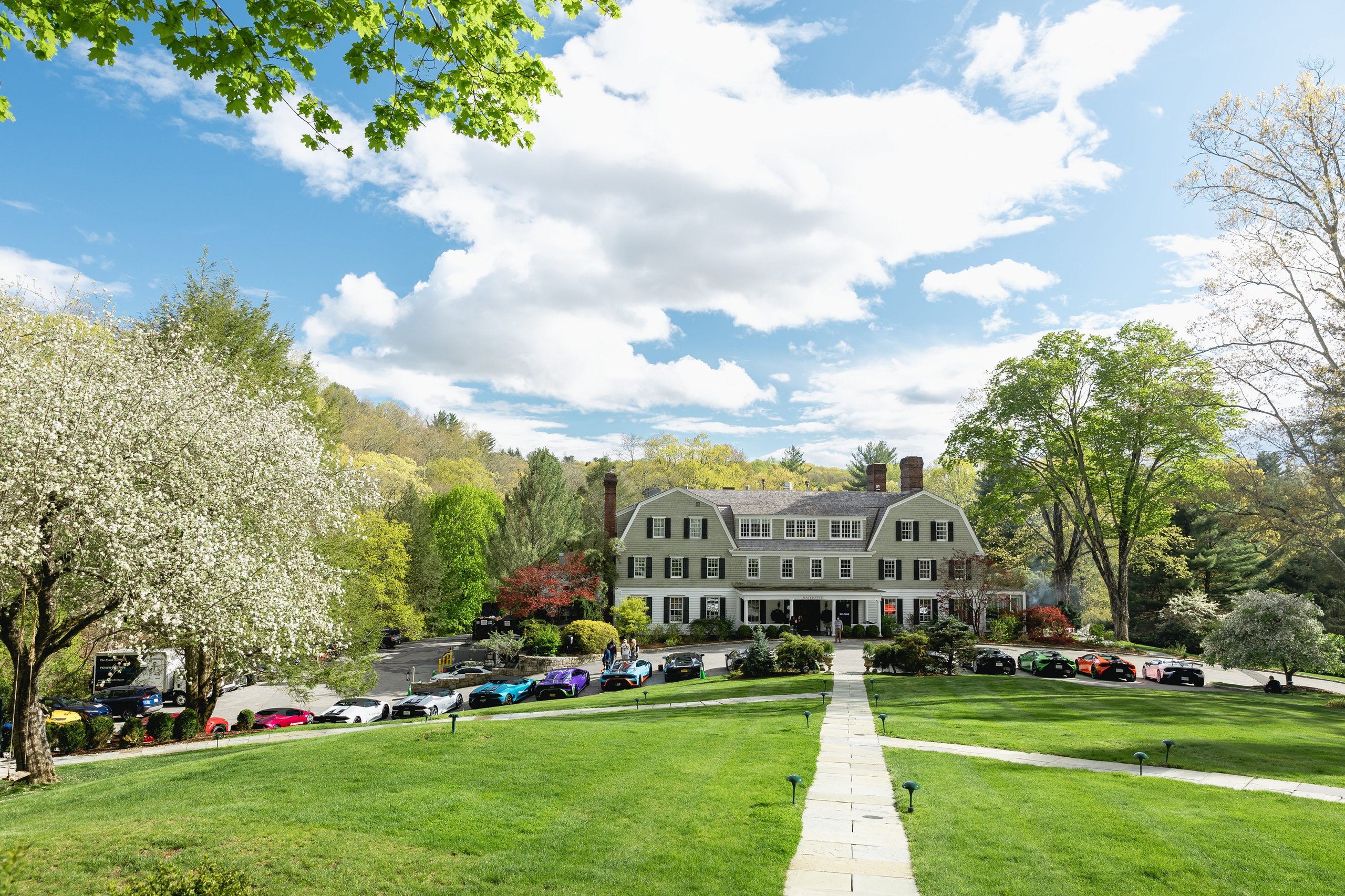 Shedrivesalambo: How Lamborghini Built A Supercar Community No Rival Bothered To Create 5 Grand estate house surrounded by greenery and blooming trees with numerous colorful lamborghinis parked in front