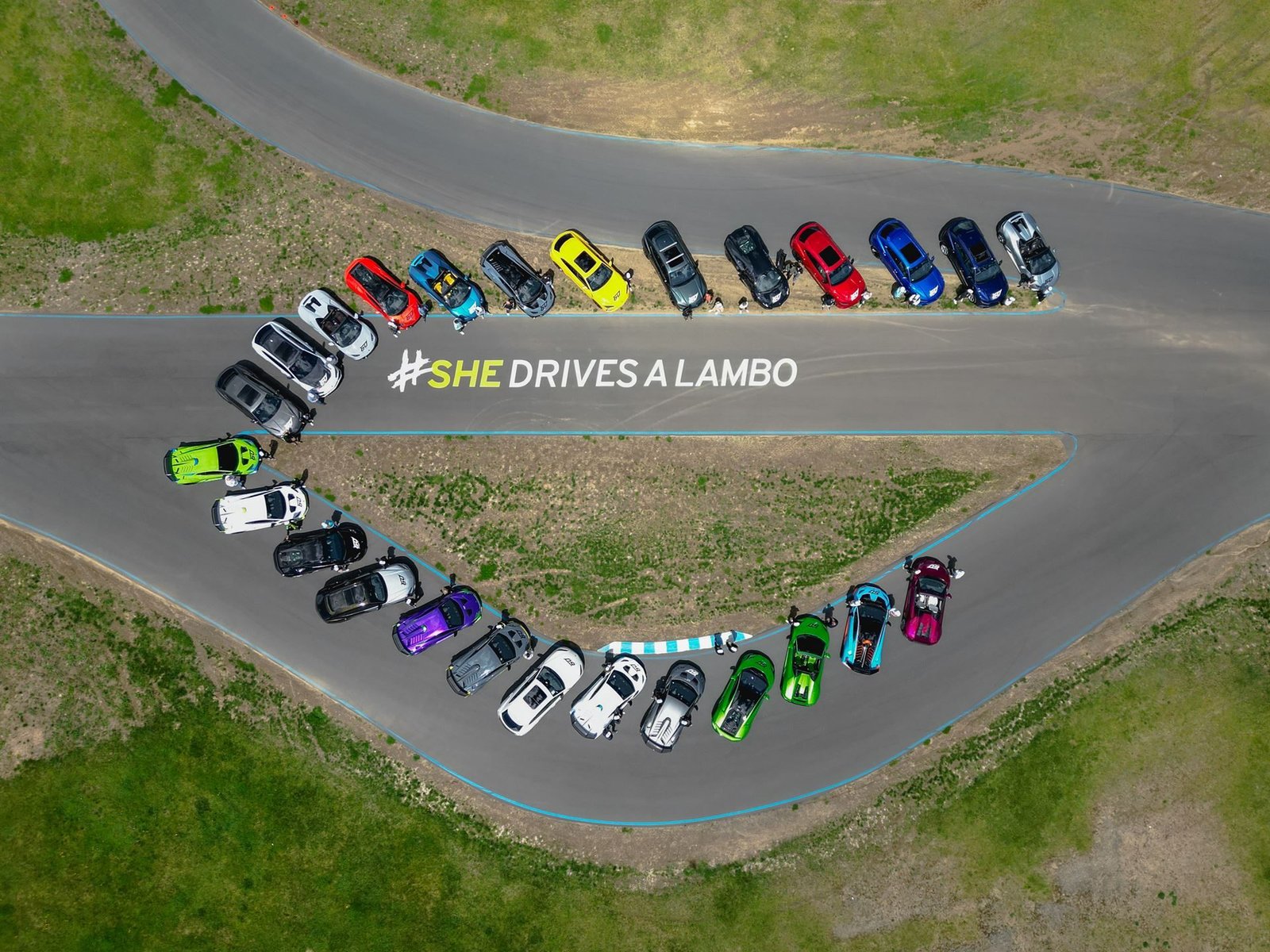 Aerial view of Lamborghini cars arranged in a semi-circle on a race track with the hashtag SHEdrivesalambo spelled out in the center
