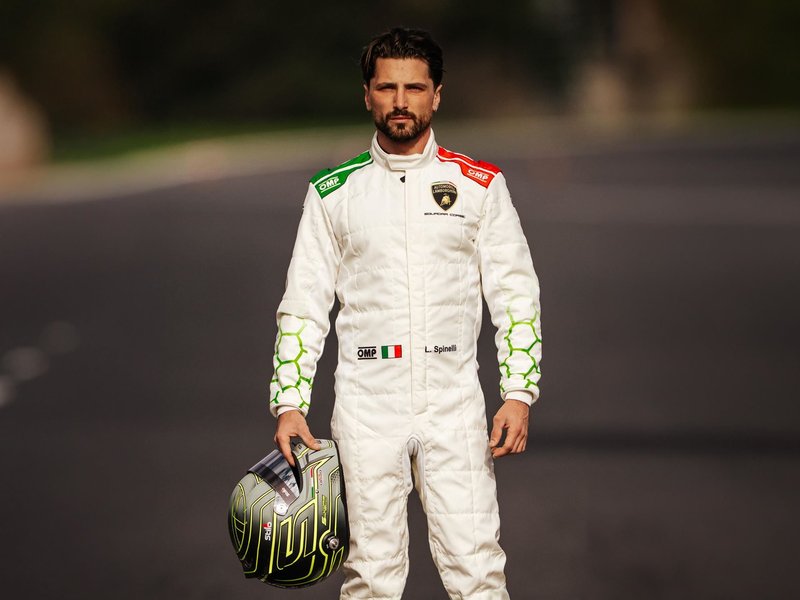 Loris Spinelli standing on a race track in his Lamborghini Squadra Corse racing suit, holding his helmet