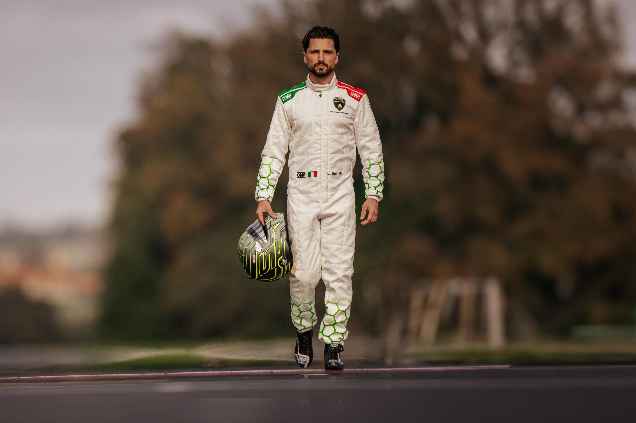 Loris Spinelli Joins Lamborghini Squadra Corse As Factory Driver For 2024 3 Loris spinelli walking along a race track holding his helmet, wearing a lamborghini squadra corse racing suit with italian flag color accents