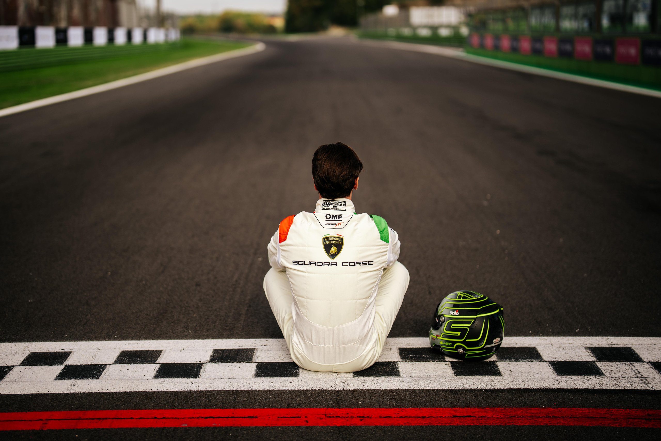 Loris Spinelli Joins Lamborghini Squadra Corse As Factory Driver For 2024 5 Loris spinelli sitting on the starting line of a race track facing away from camera, helmet beside him, lamborghini squadra corse logo visible on his racing suit