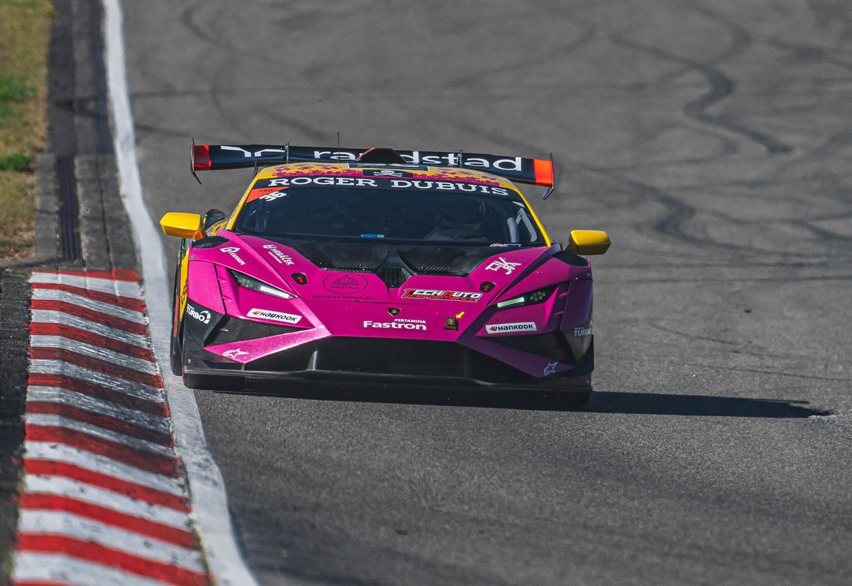 A vibrant pink and yellow lamborghini huracán super trofeo evo2 navigating a turn on a sunny race track