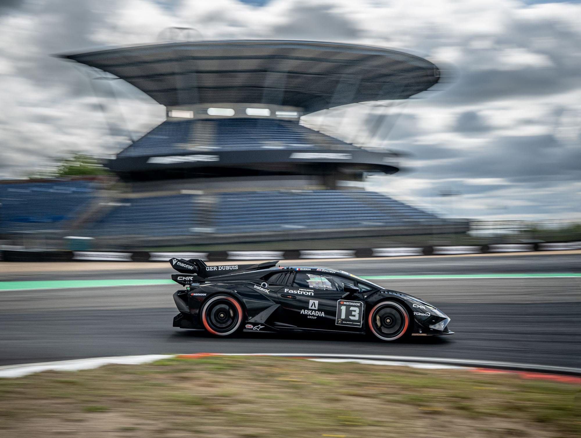 A black lamborghini huracán super trofeo evo2 at speed on track with blurred grandstand in background conveying motion
