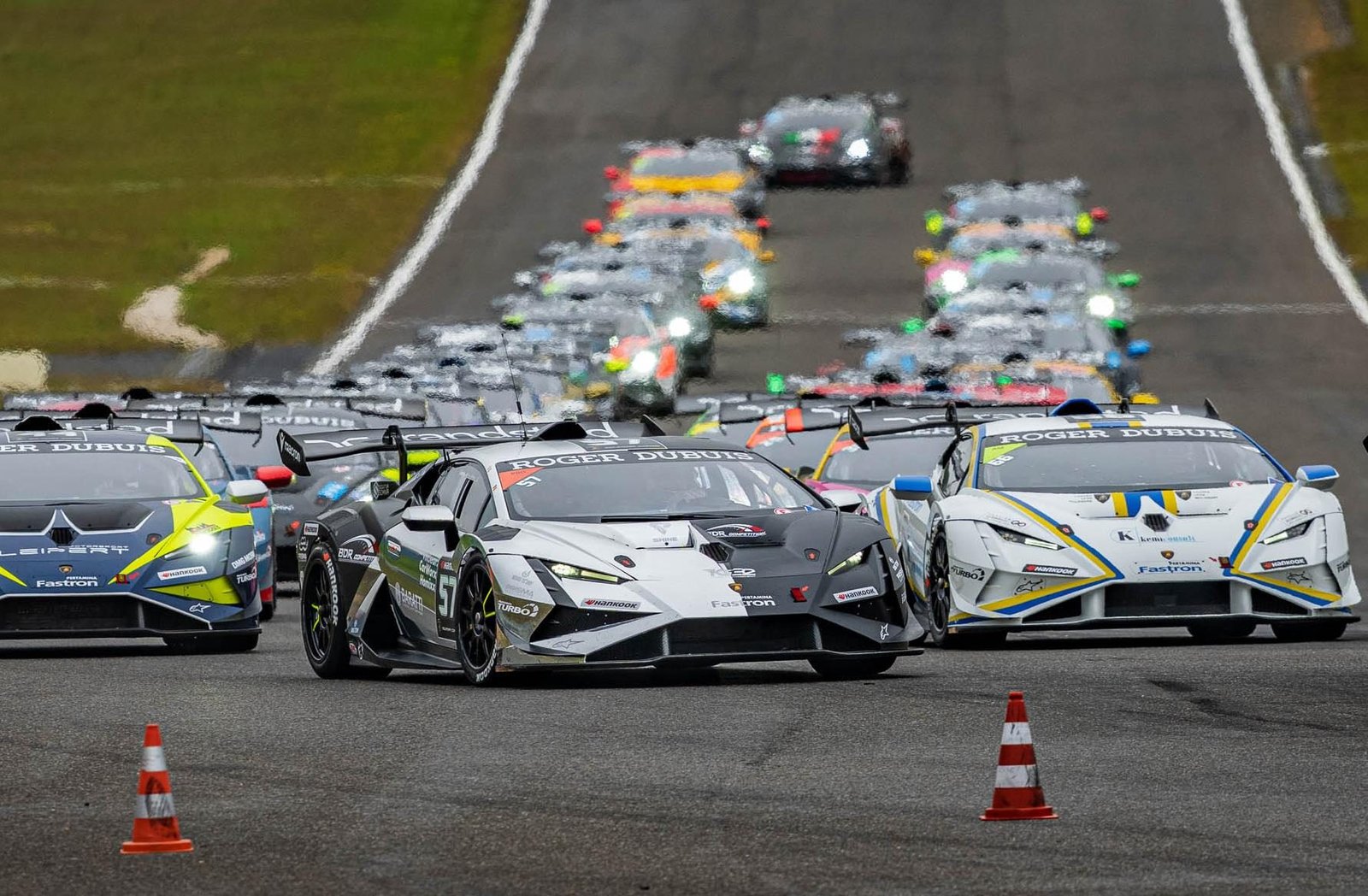 A pack of Lamborghini Huracán Super Trofeo EVO2 race cars lined up on a race track grid, led by a white and black liveried car