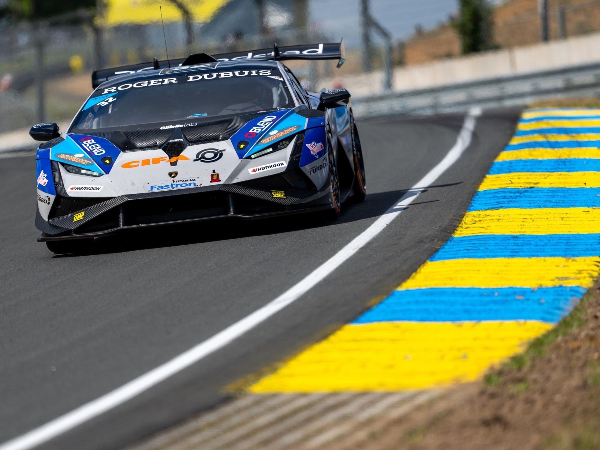 Super Trofeo Europe Hits The Nürburgring With A 1.5-Point Pro Title Fight 9 Close-up of a white and blue lamborghini huracán super trofeo evo2 navigating a turn with yellow and blue curbing prominent