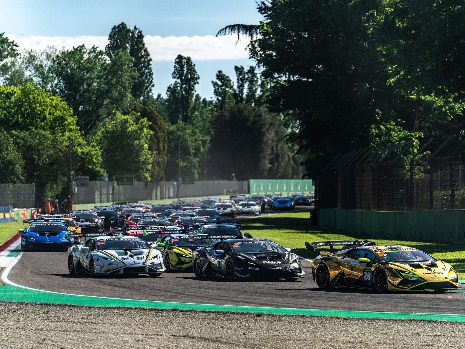 Multiple Lamborghini Huracán Super Trofeo EVO2 race cars navigating a turn during a sunny race weekend