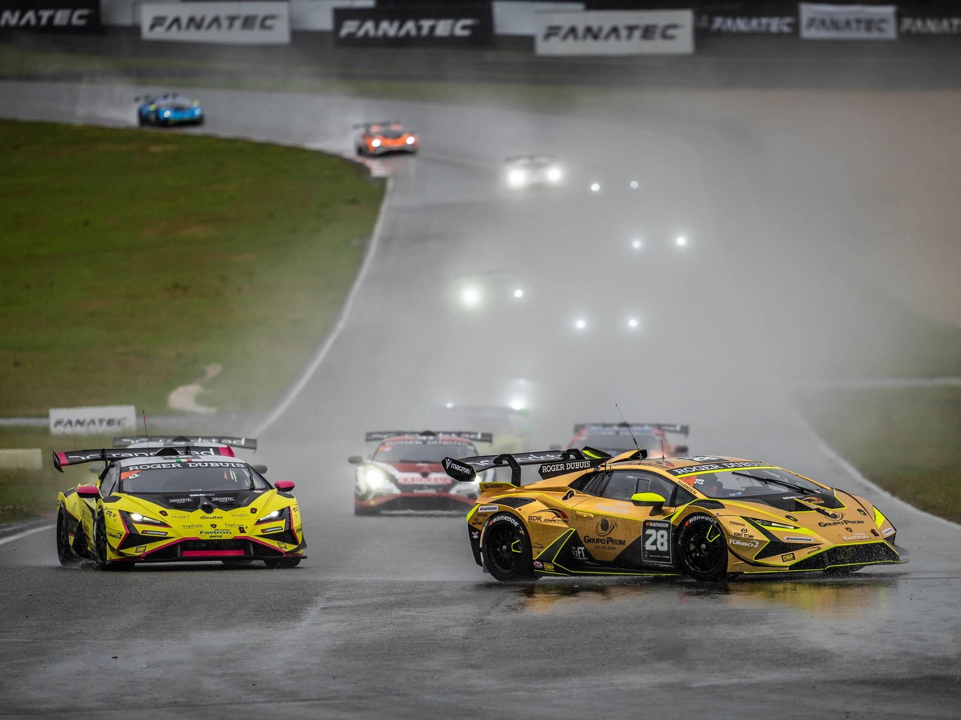 Split Weather, Split Winners: Bonduel And Orudzhev Trade Nürburgring Victories In Super Trofeo Europe 3 Two yellow lamborghini huracán super trofeo evo race cars lead a pack on a wet track with headlights piercing through mist and spray