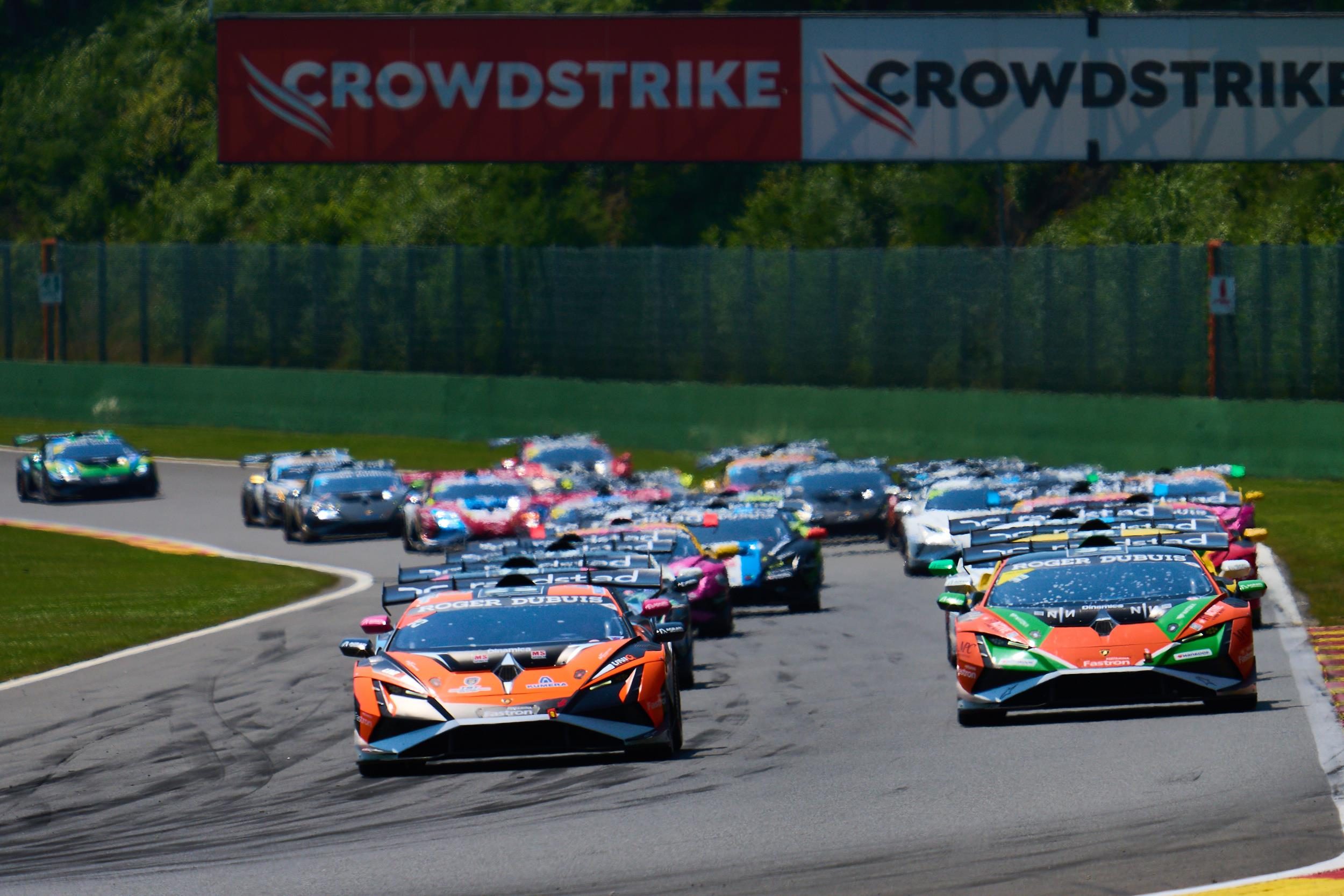 Two lamborghini huracán super trofeo evo2 race cars leading a pack on track at spa-francorchamps with a crowdstrike banner visible
