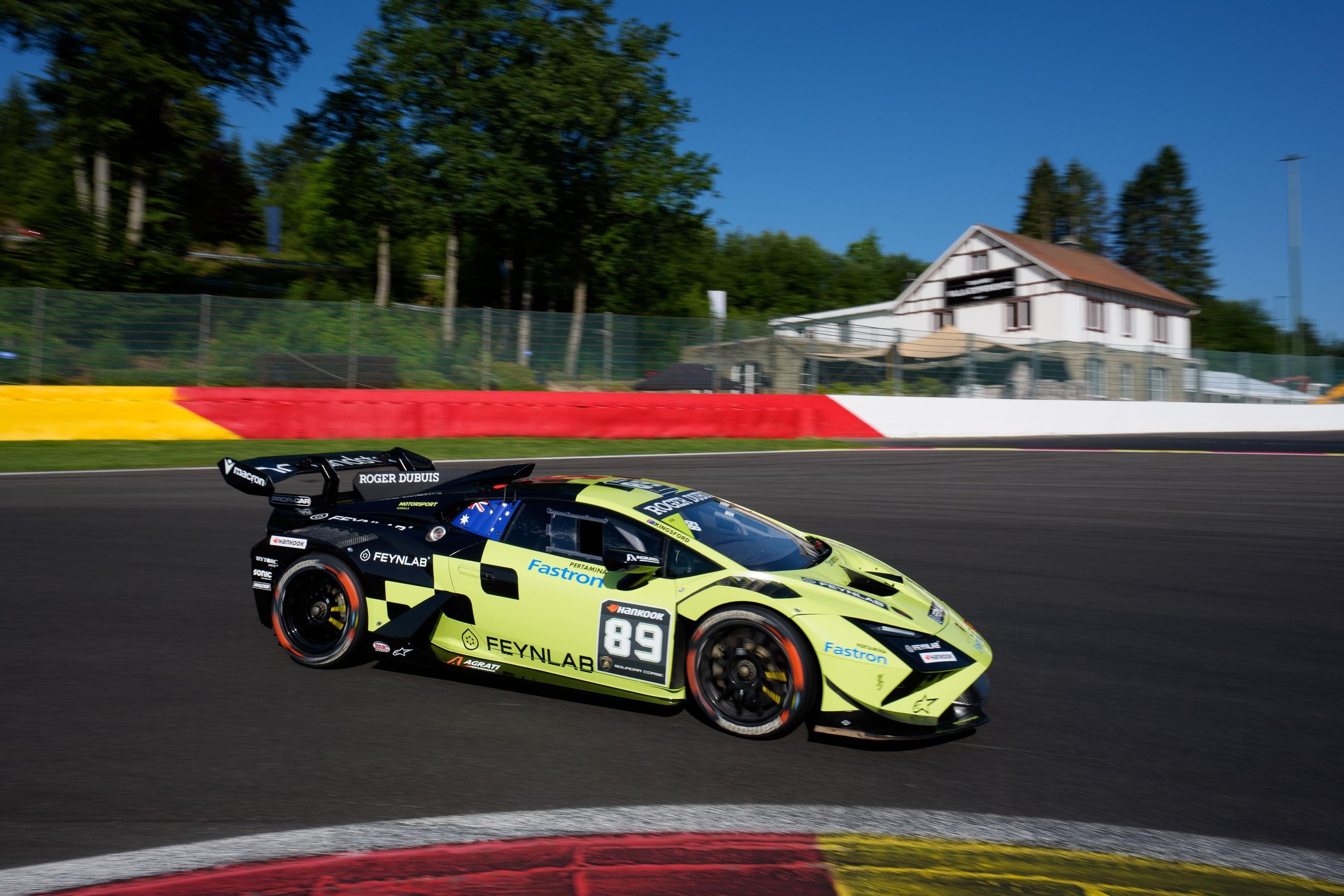 A lime green and black lamborghini huracán super trofeo evo2 number 89 speeding through a corner under clear blue skies at spa-francorchamps