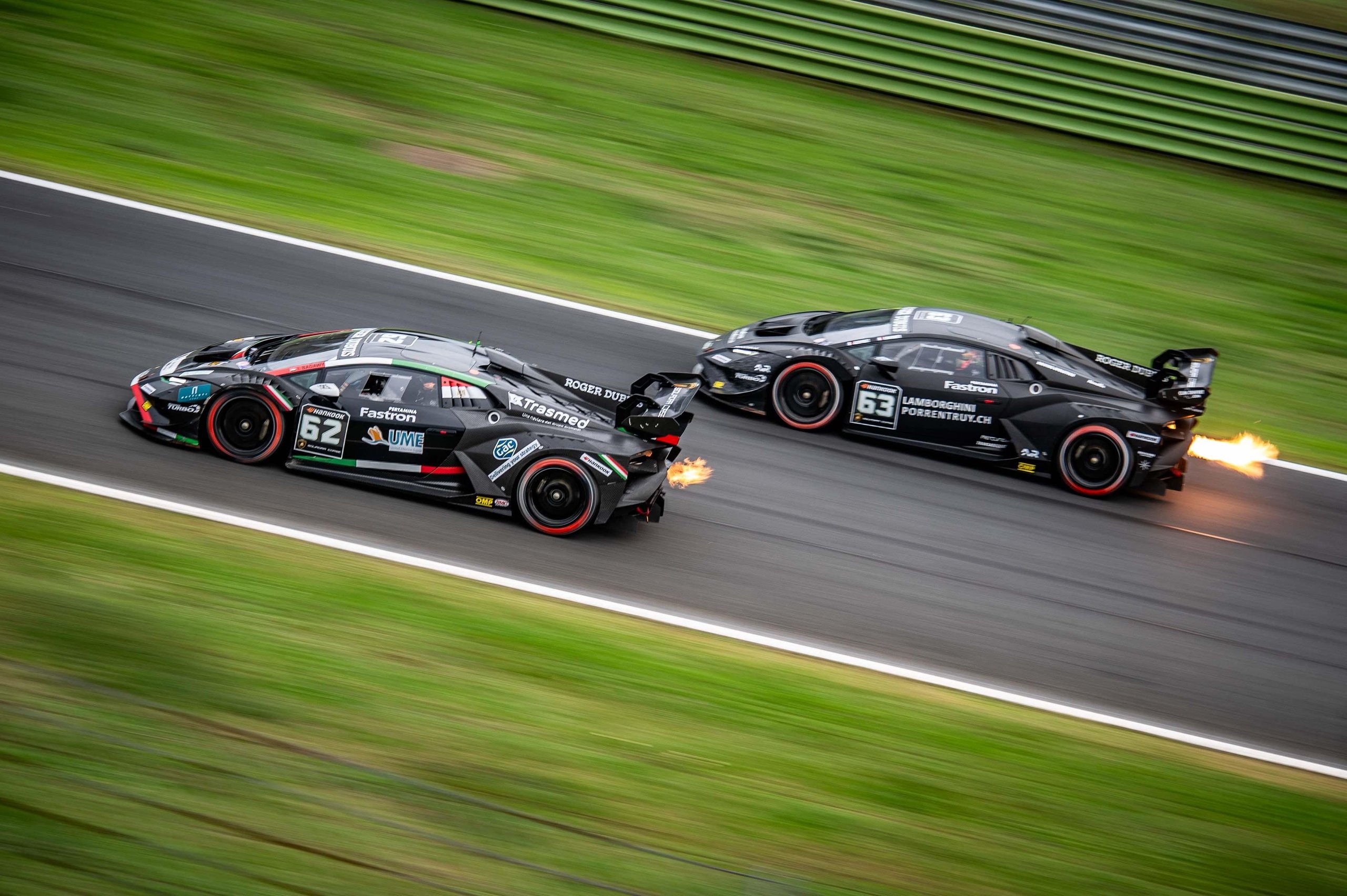 Fifty Cars, Four Open Championships, And One Week Left: Super Trofeo Europe'S Vallelunga Showdown 5 Two black lamborghini huracán super trofeo evo2 race cars in close battle on track, one trailing exhaust flames