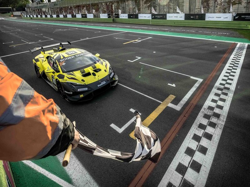 A yellow and black Lamborghini Huracán Super Trofeo EVO2 crosses the finish line under a checkered flag at Vallelunga