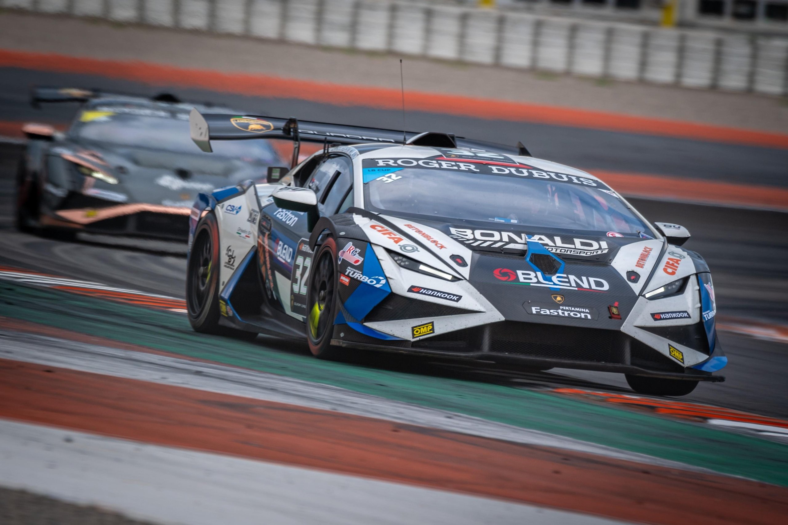 52 Huracán Evo2S At Vallelunga: Why The Super Trofeo'S Record Grid Matters Beyond The Championship Fight 5 A white and blue liveried lamborghini huracán super trofeo evo2 leads another car at speed on a racetrack