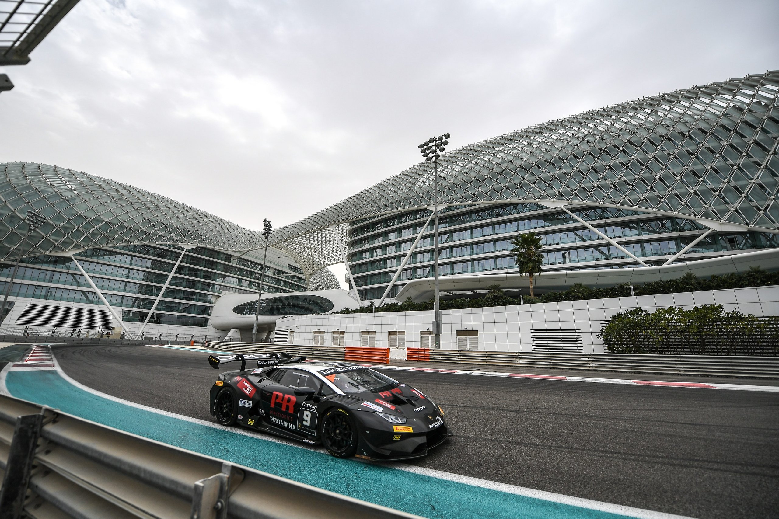 Black lamborghini huracán super trofeo evo race car number 9 on track with futuristic buildings in the background