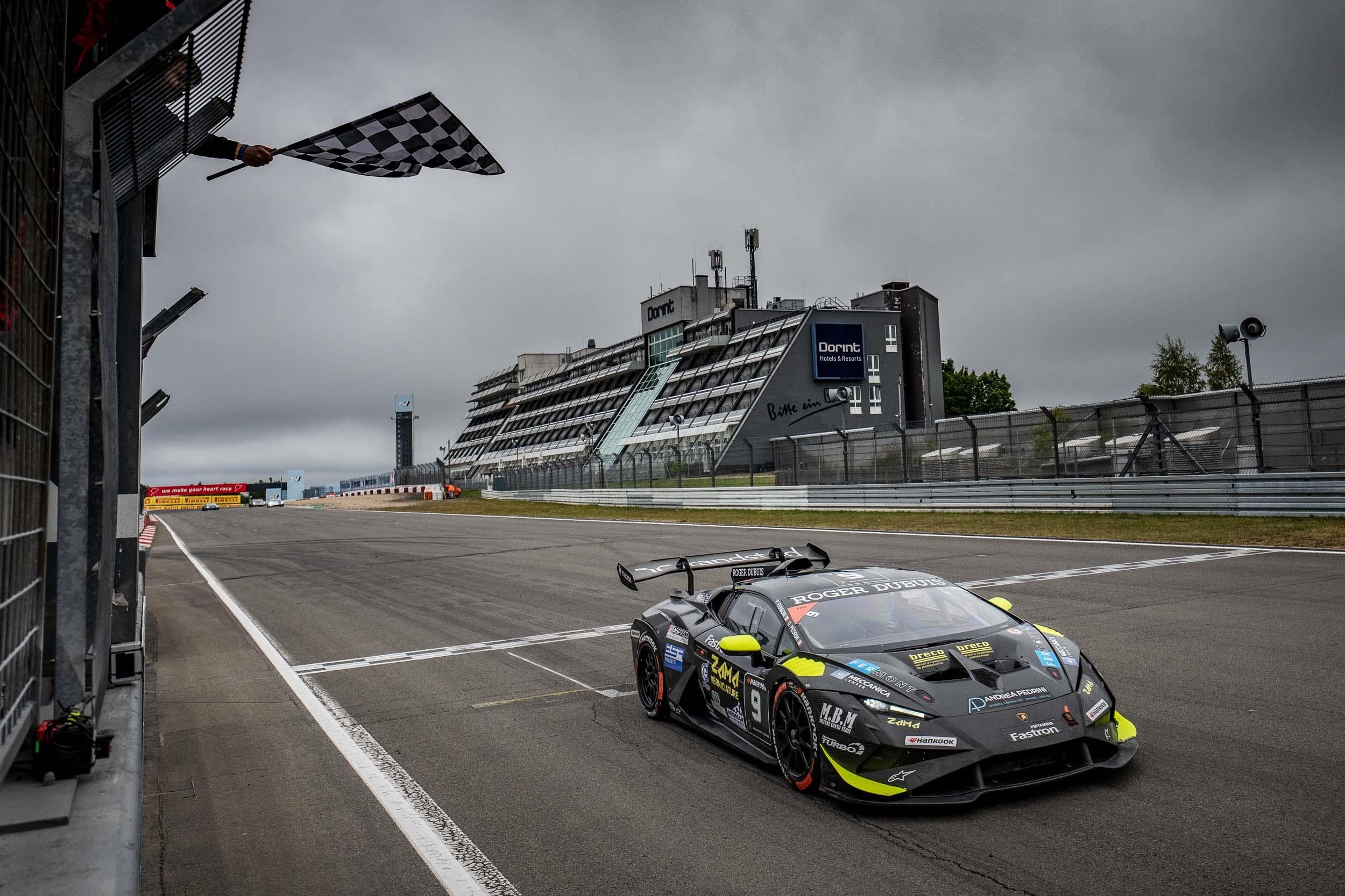 A grey lamborghini huracán super trofeo evo2 crossing the finish line under a waving checkered flag at the nürburgring