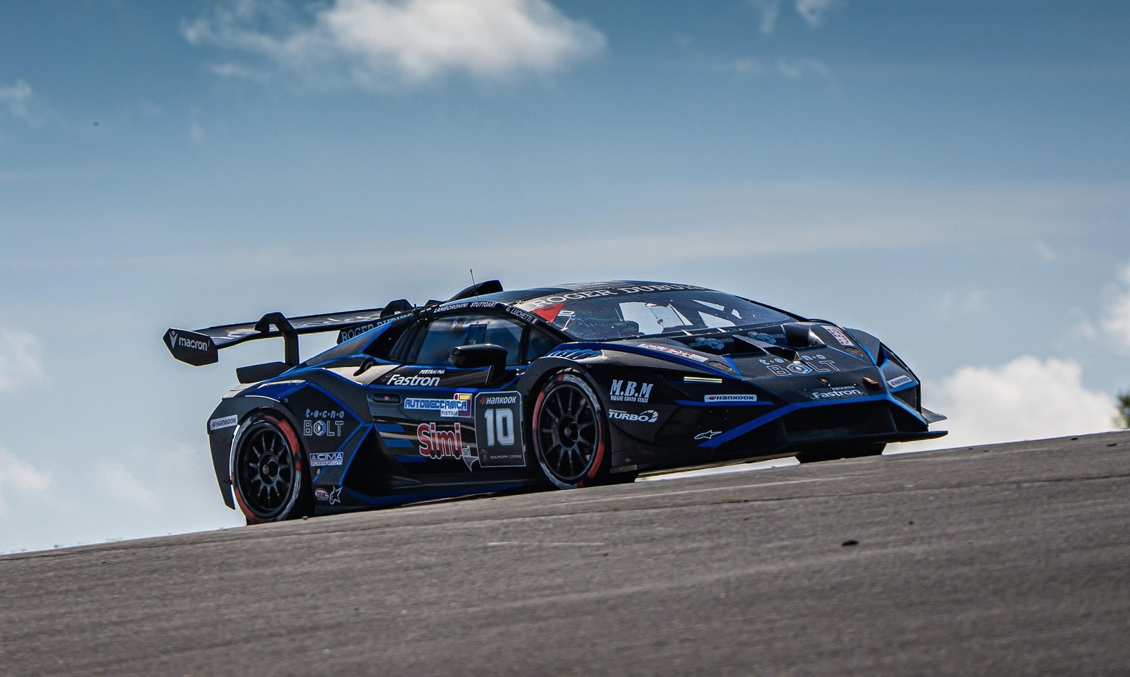 A black Lamborghini Huracán Super Trofeo EVO2 cornering on the Nürburgring circuit under partly cloudy skies