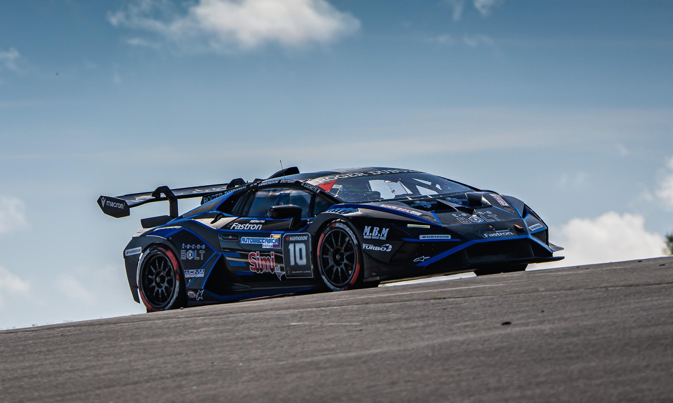 A black lamborghini huracán super trofeo evo2 cornering on the nürburgring circuit under partly cloudy skies